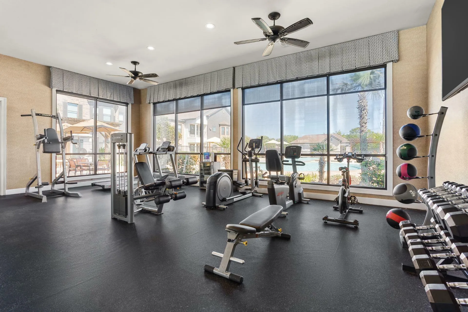 Bright and modern fitness center with large windows, equipped with cardio machines, weights, and exercise bikes offering a refreshing outdoor pool view.