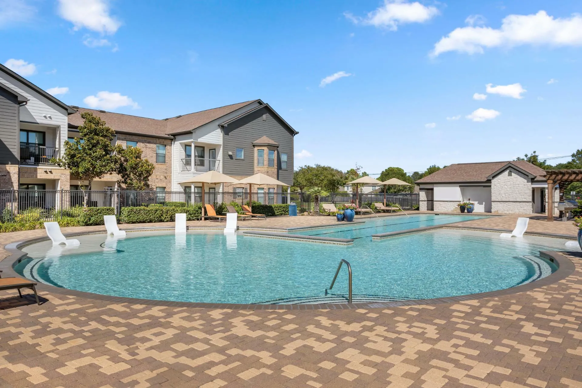 Inviting apartment complex with a sparkling pool, elegant lounge chairs, and vibrant landscaped gardens under a clear blue sky.