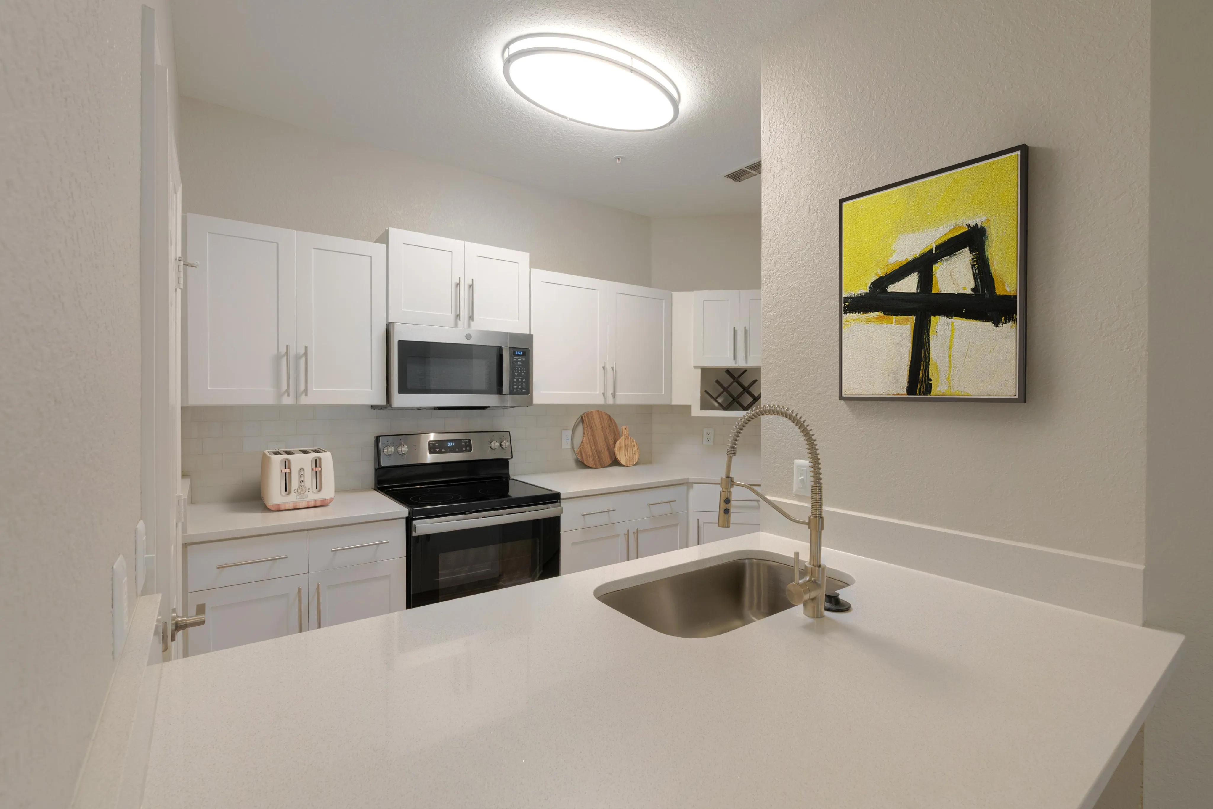 Modern kitchen with sleek white cabinetry, stainless steel appliances, and elegant countertops, enhanced by bright artistic decor.