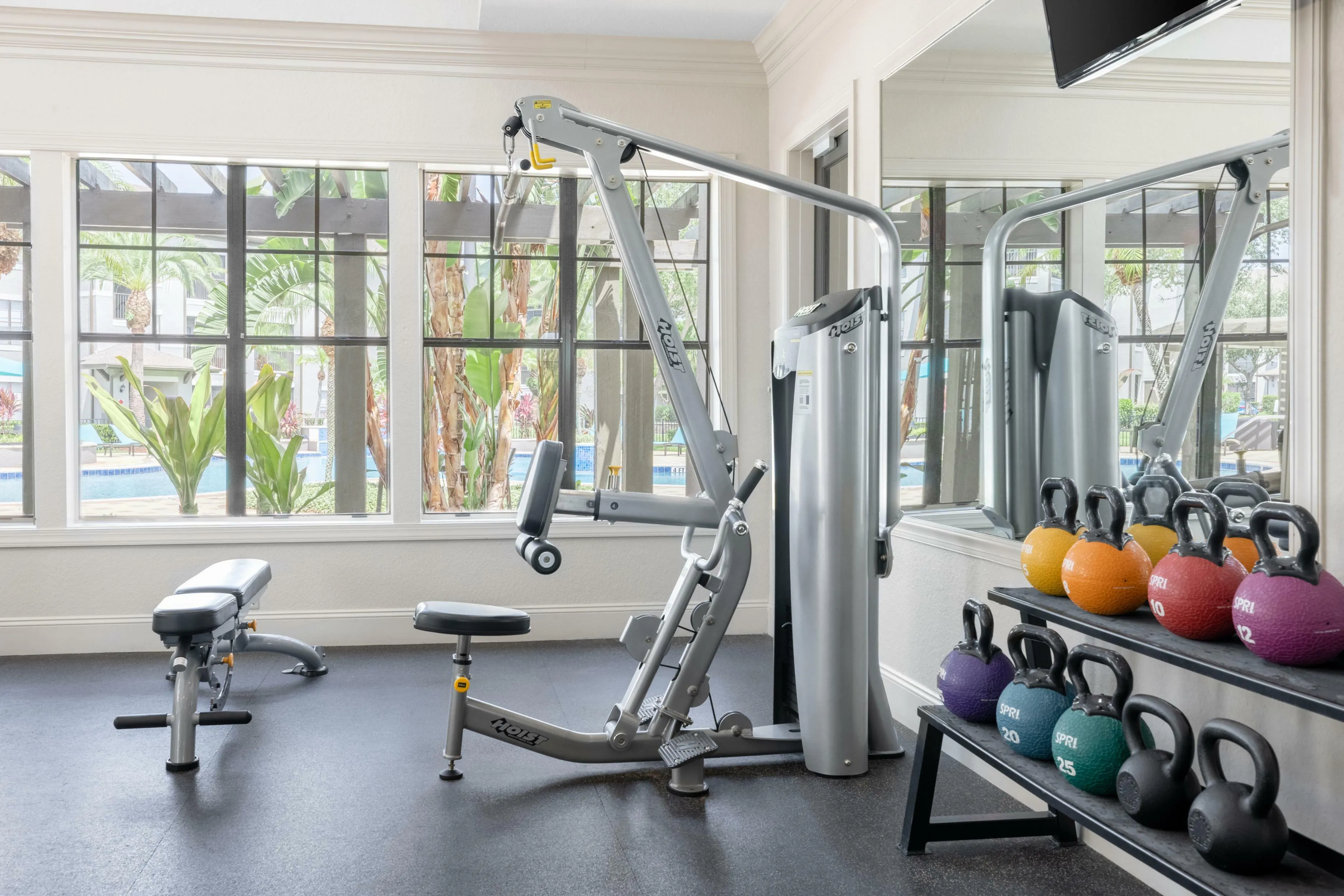 Inviting gym space with modern exercise equipment and vibrant kettlebells, overlooking lush outdoor views.