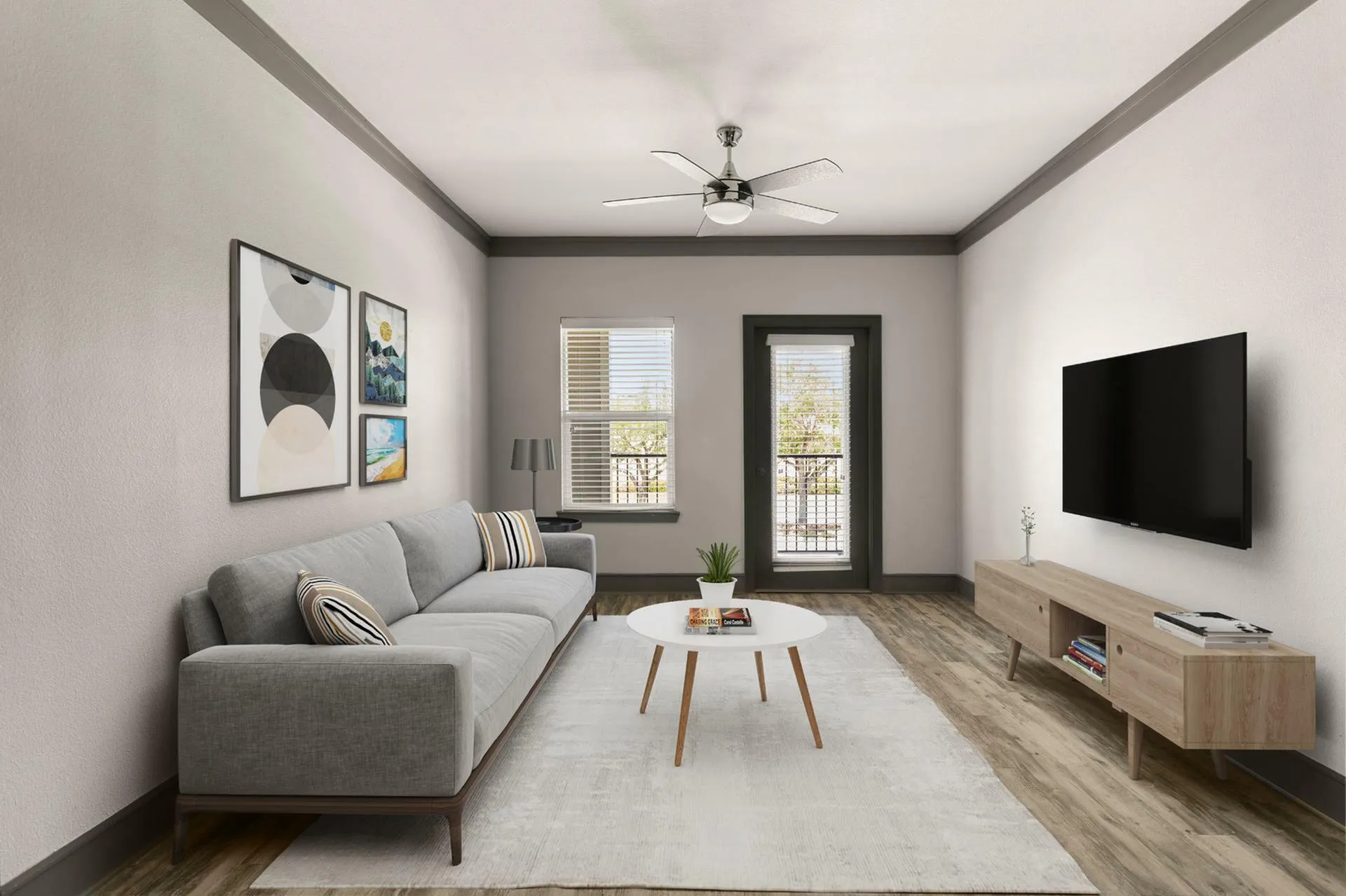 Chic and modern living room featuring a sleek gray sofa, contemporary art, large flat-screen TV, and elegant wooden flooring. Natural light enhances the open space through a window and door.