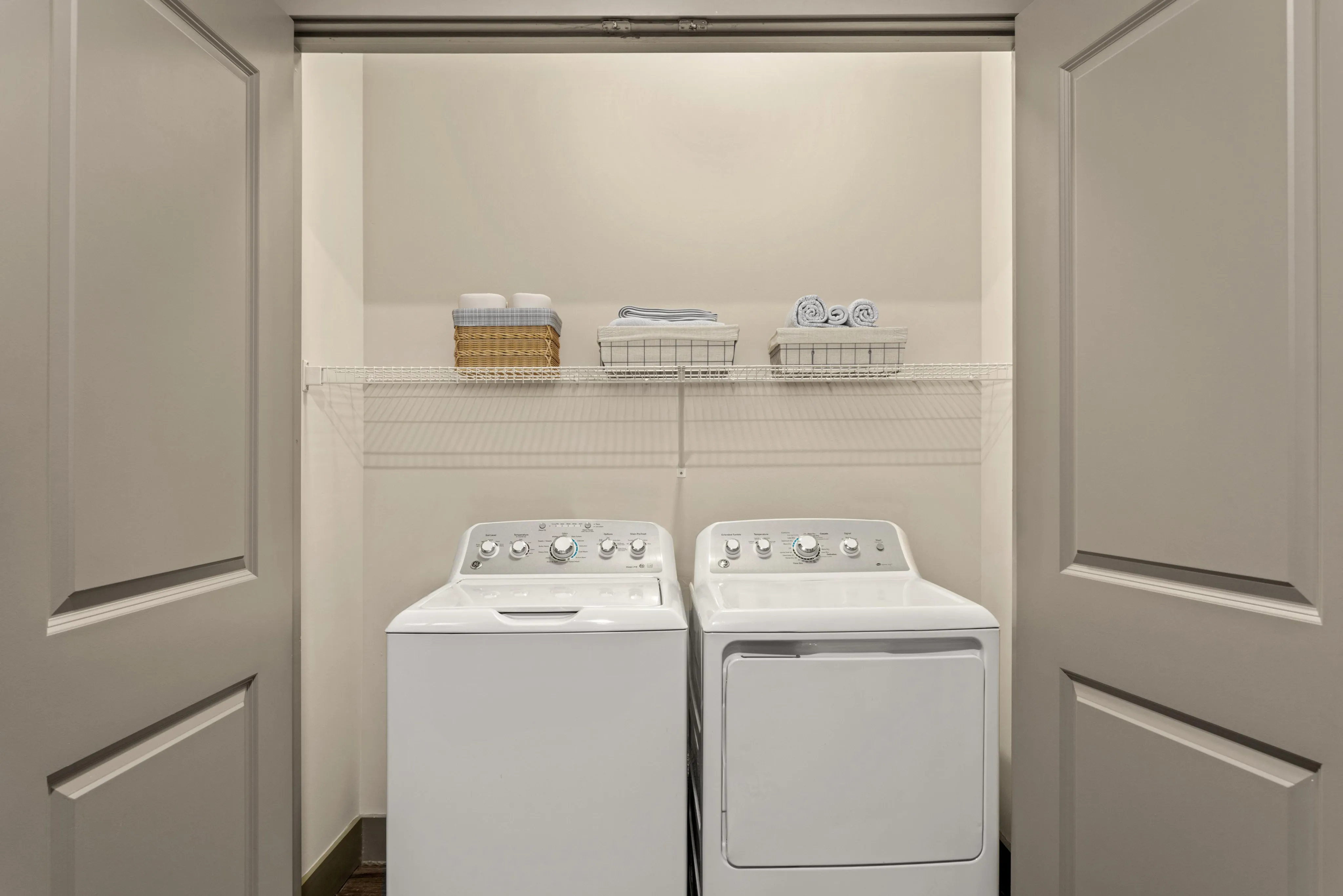 Compact laundry room featuring modern washer and dryer with convenient shelving for organized storage.