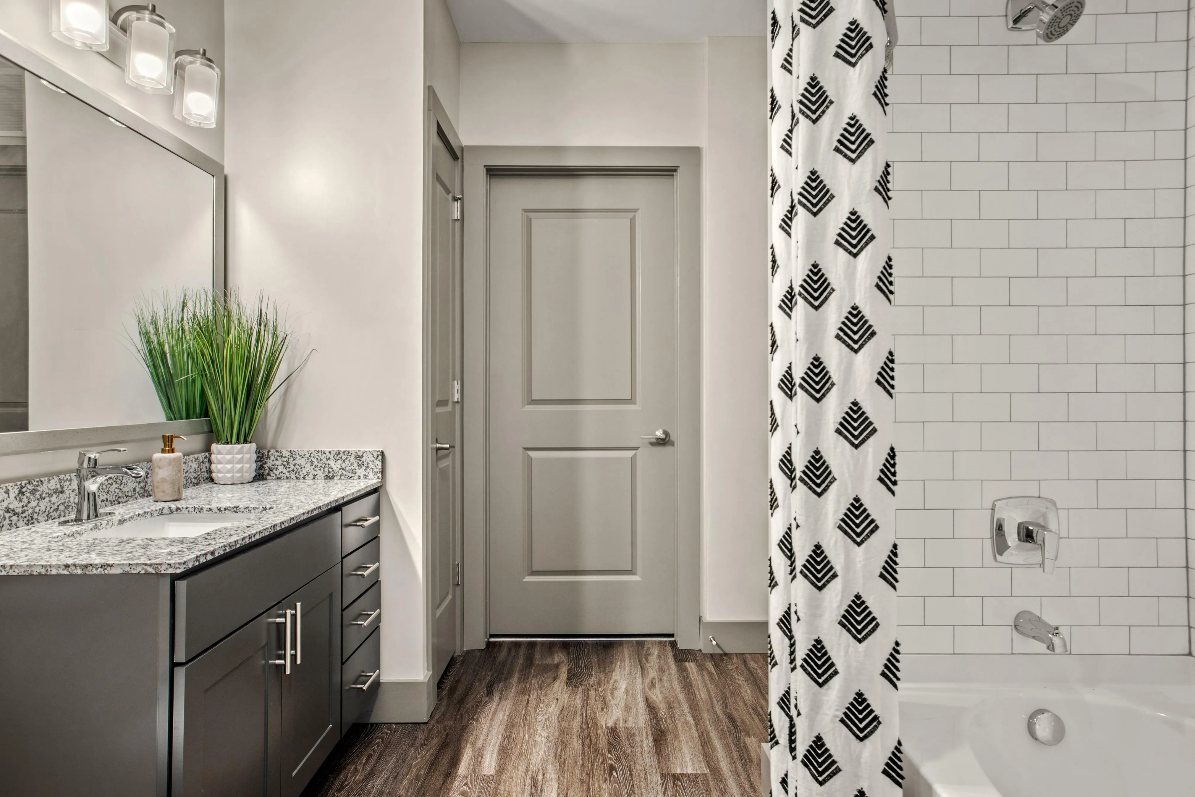 Modern bathroom with sleek granite countertop, elegant dark cabinetry, and stylish tile accents, featuring a contemporary bathtub and vibrant decor.