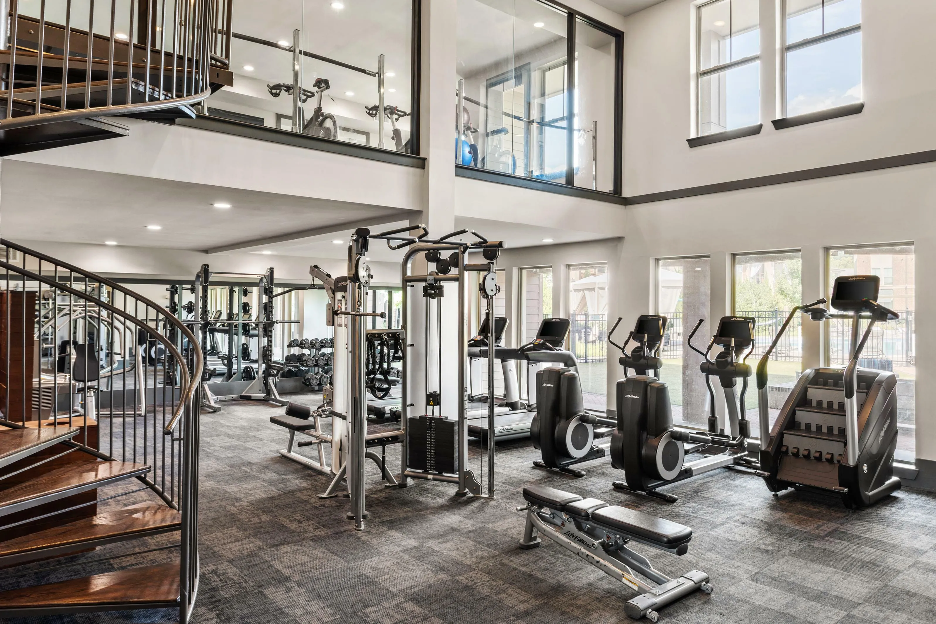 Luxurious fitness center with modern cardio machines, weight training equipment, and elegant spiral staircase.