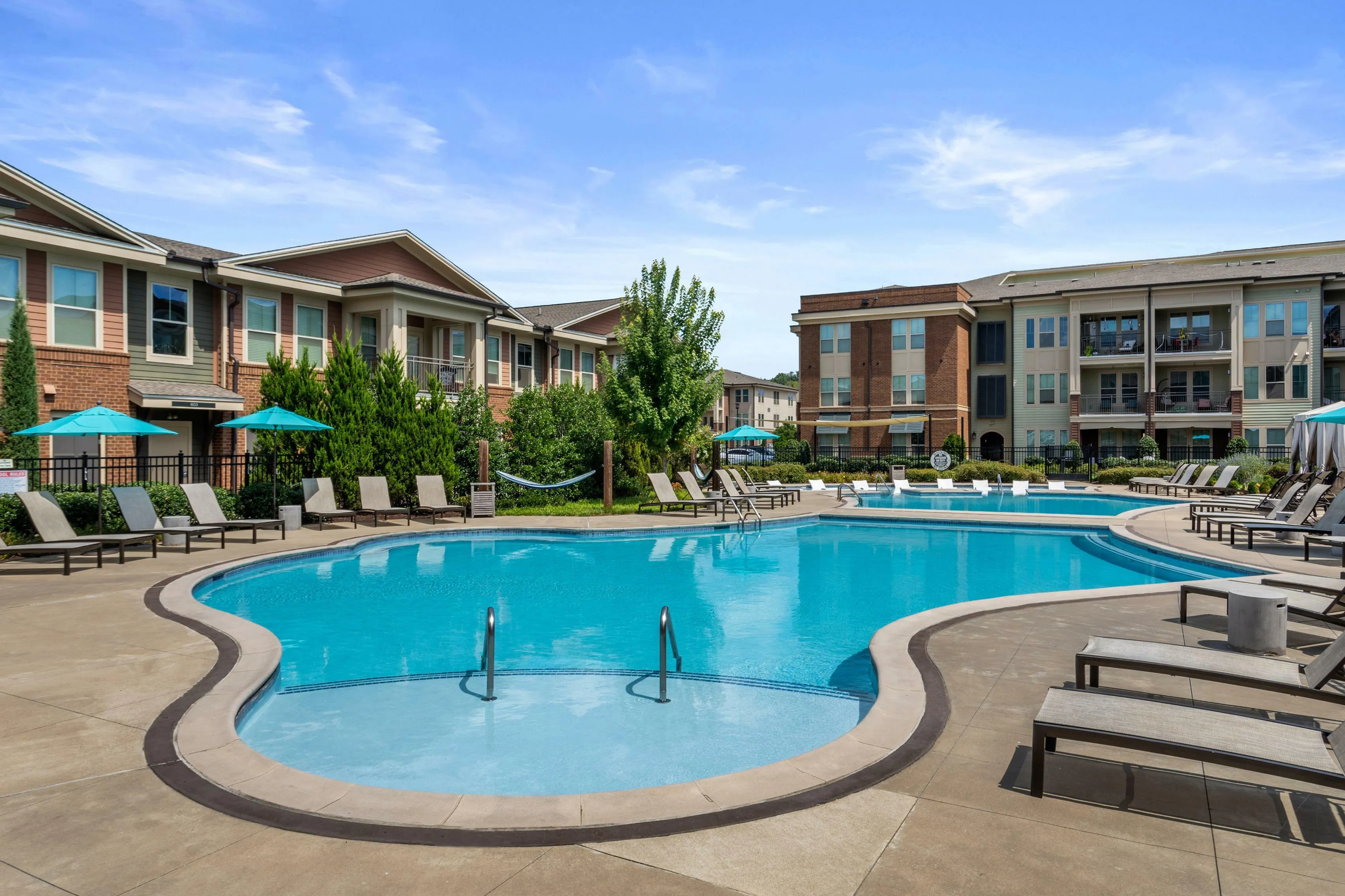 Luxurious apartment complex featuring a sparkling resort-style pool surrounded by comfortable lounge chairs and vibrant umbrellas, perfect for relaxation and entertainment.