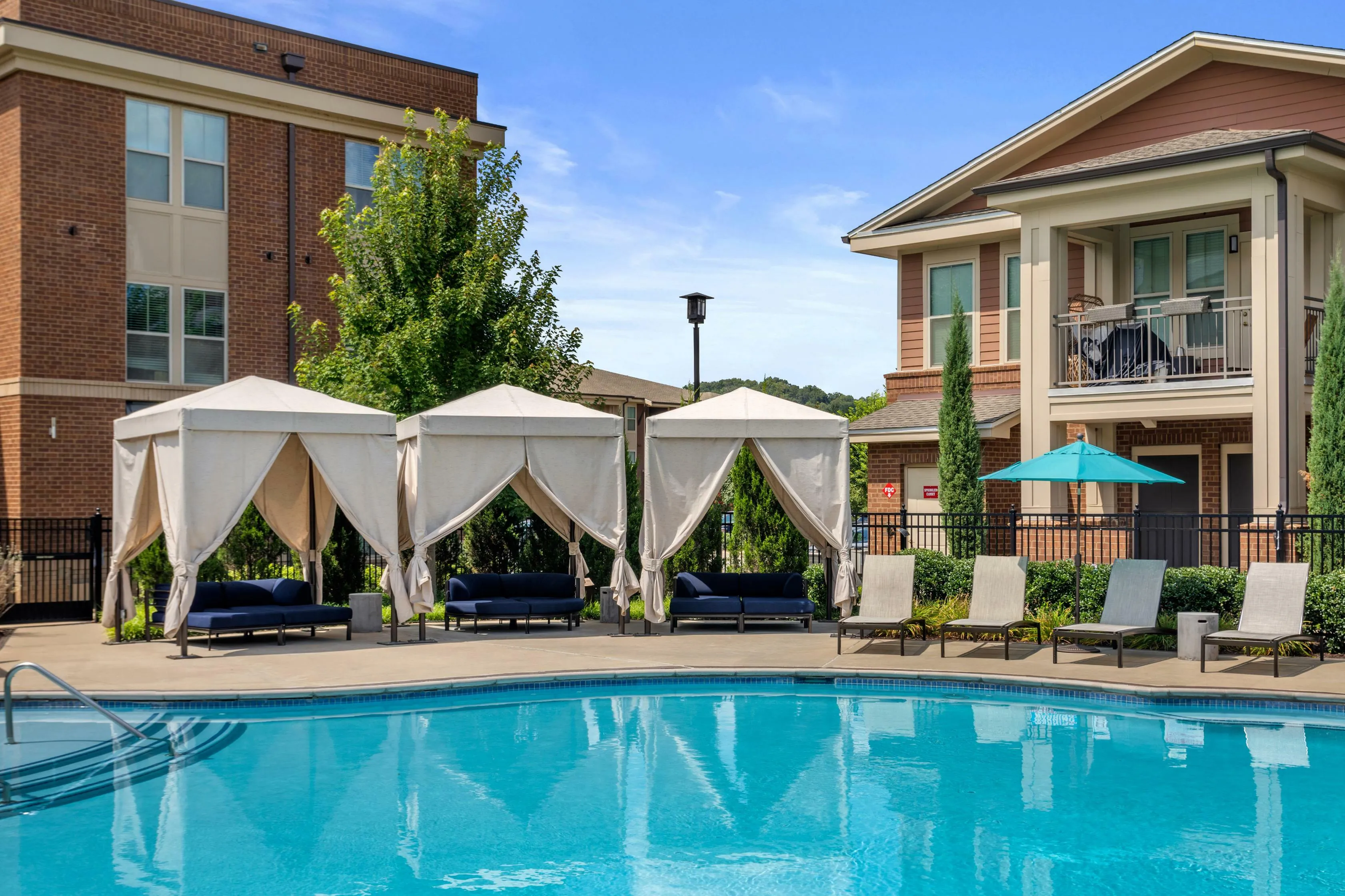 Luxurious apartment pool area with elegant cabanas and sun loungers, perfect for relaxation and leisure under a clear blue sky.