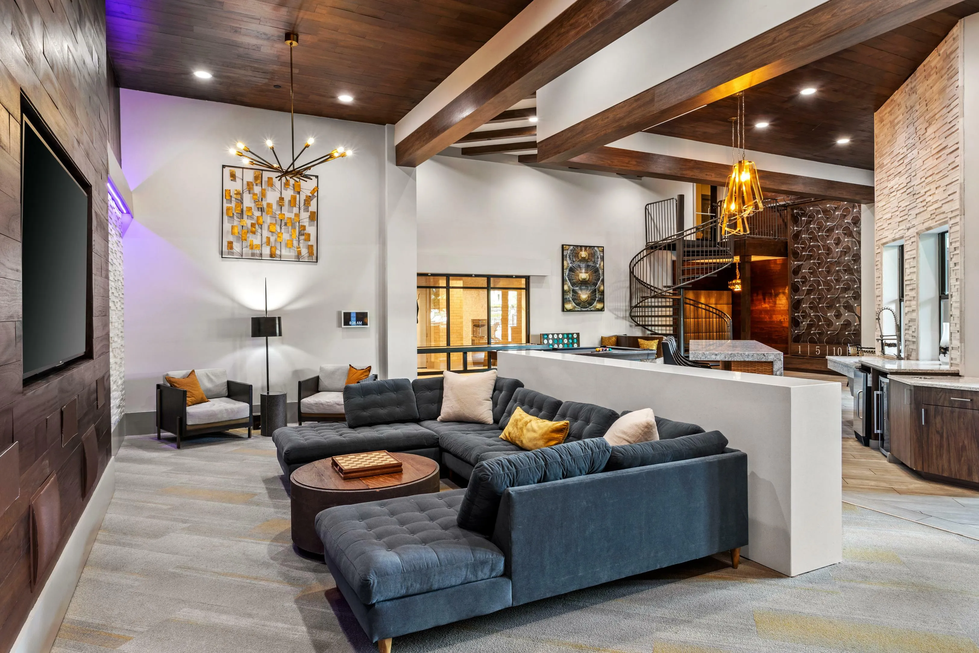 Luxurious open-concept living space featuring a stylish spiral staircase, elegant modern chandelier, plush sectional sofa, and cozy lounge area with contemporary decor.