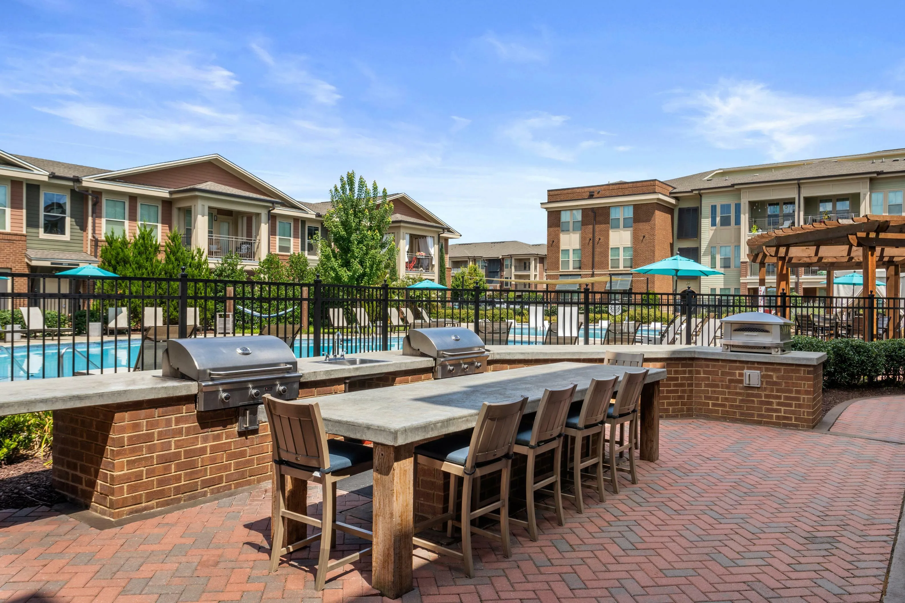 Inviting outdoor area featuring modern barbecue grills, a spacious dining counter, and a view of luxurious apartment amenities including a sparkling pool and elegant architecture.