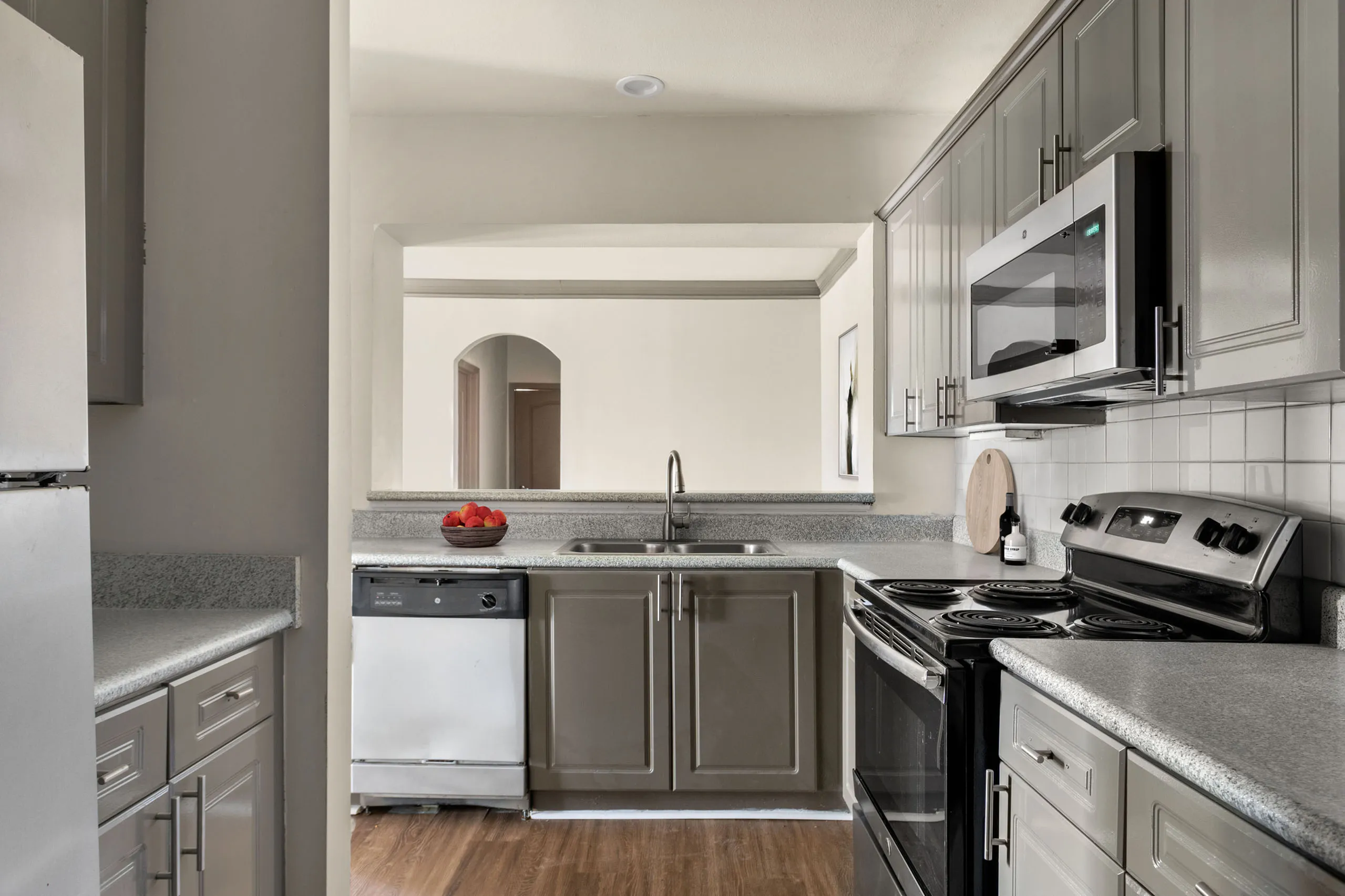 Bright and inviting kitchen featuring sleek gray cabinets, stainless steel appliances, and a cozy breakfast bar with a bowl of fresh fruit adding a pop of color.