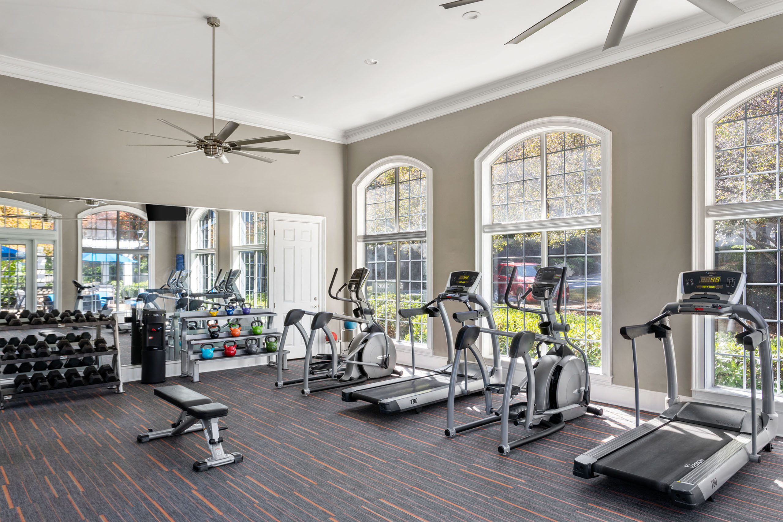 Bright and modern fitness center featuring state-of-the-art cardio equipment, free weights, and large windows for natural light.
