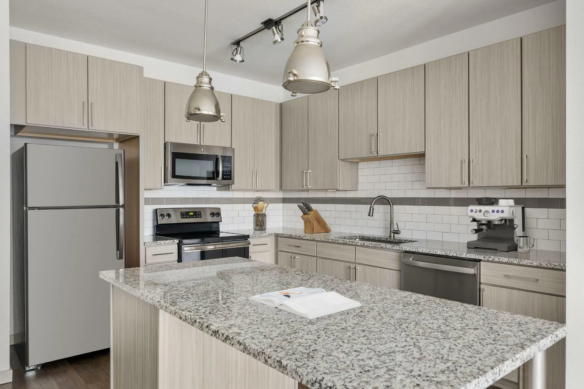 Modern kitchen with sleek granite countertops, light wood cabinets, stainless steel appliances, and stylish pendant lighting.