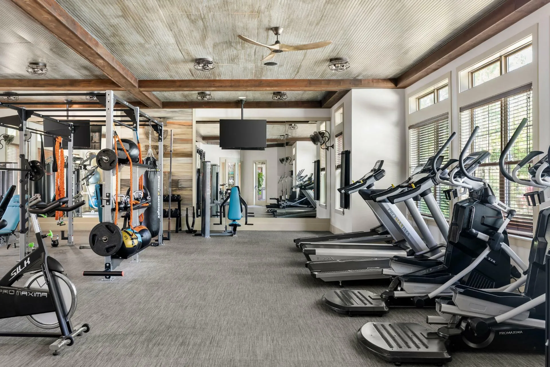 Modern fitness center with state-of-the-art gym equipment, bright windows, and a stylish ceiling fan, offering a vibrant workout environment.
