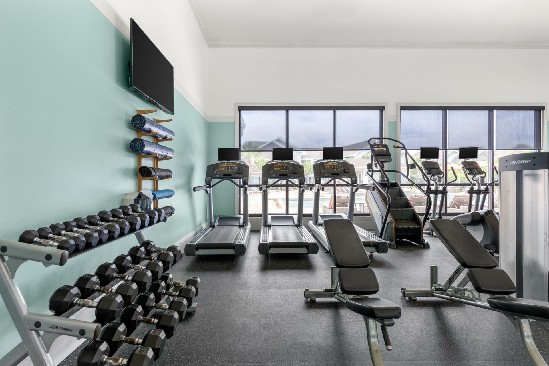 Modern fitness center with state-of-the-art treadmills, extensive free weights, and yoga mats in a stylish, well-lit space.