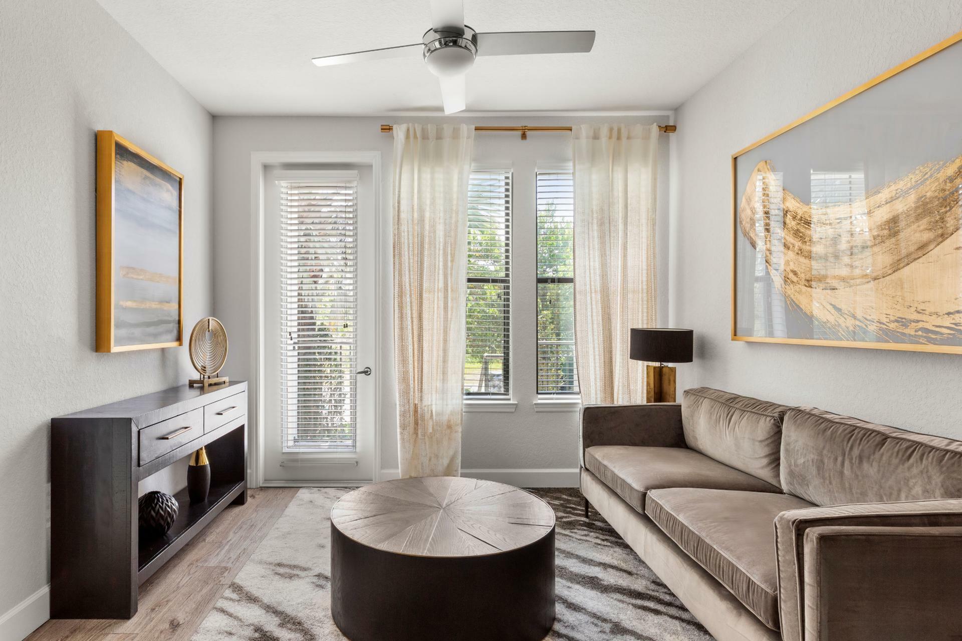Bright and inviting living room with a plush sofa, modern art, and abundant natural light from large windows.