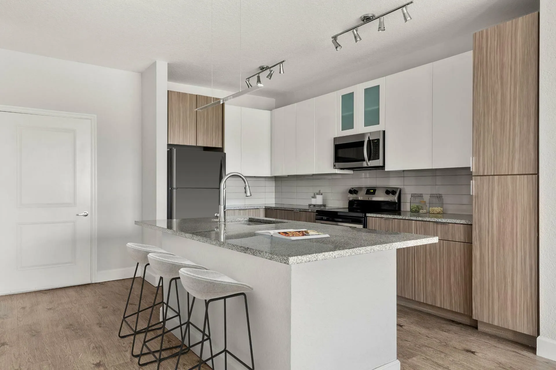 Sleek modern kitchen featuring a spacious granite island, stylish bar stools, and stainless steel appliances.