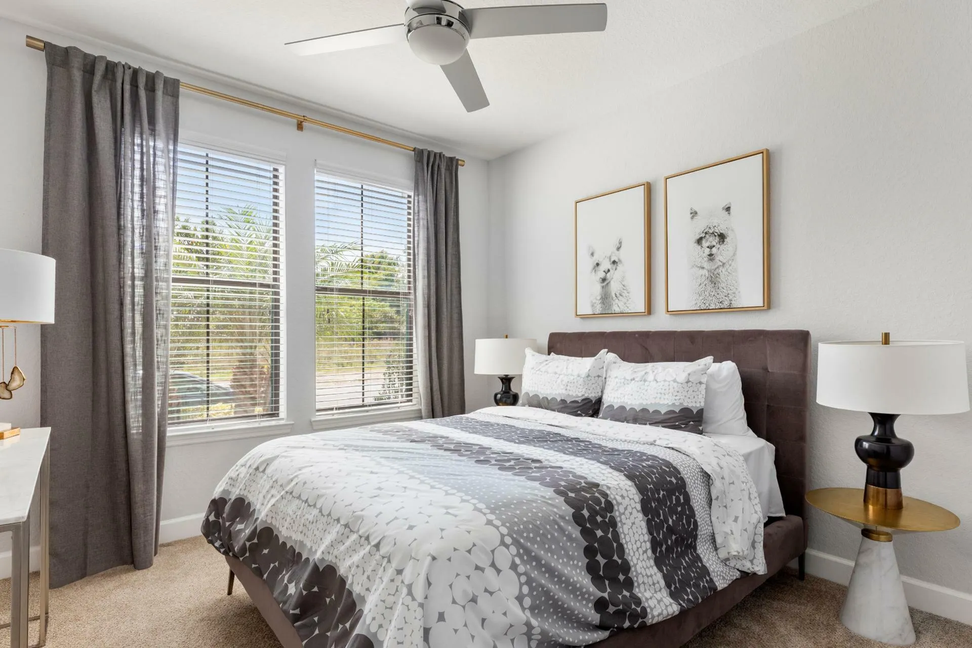 Bright and inviting bedroom featuring a plush bed with patterned bedding, elegant bedside lamps, and large windows with stylish curtains.