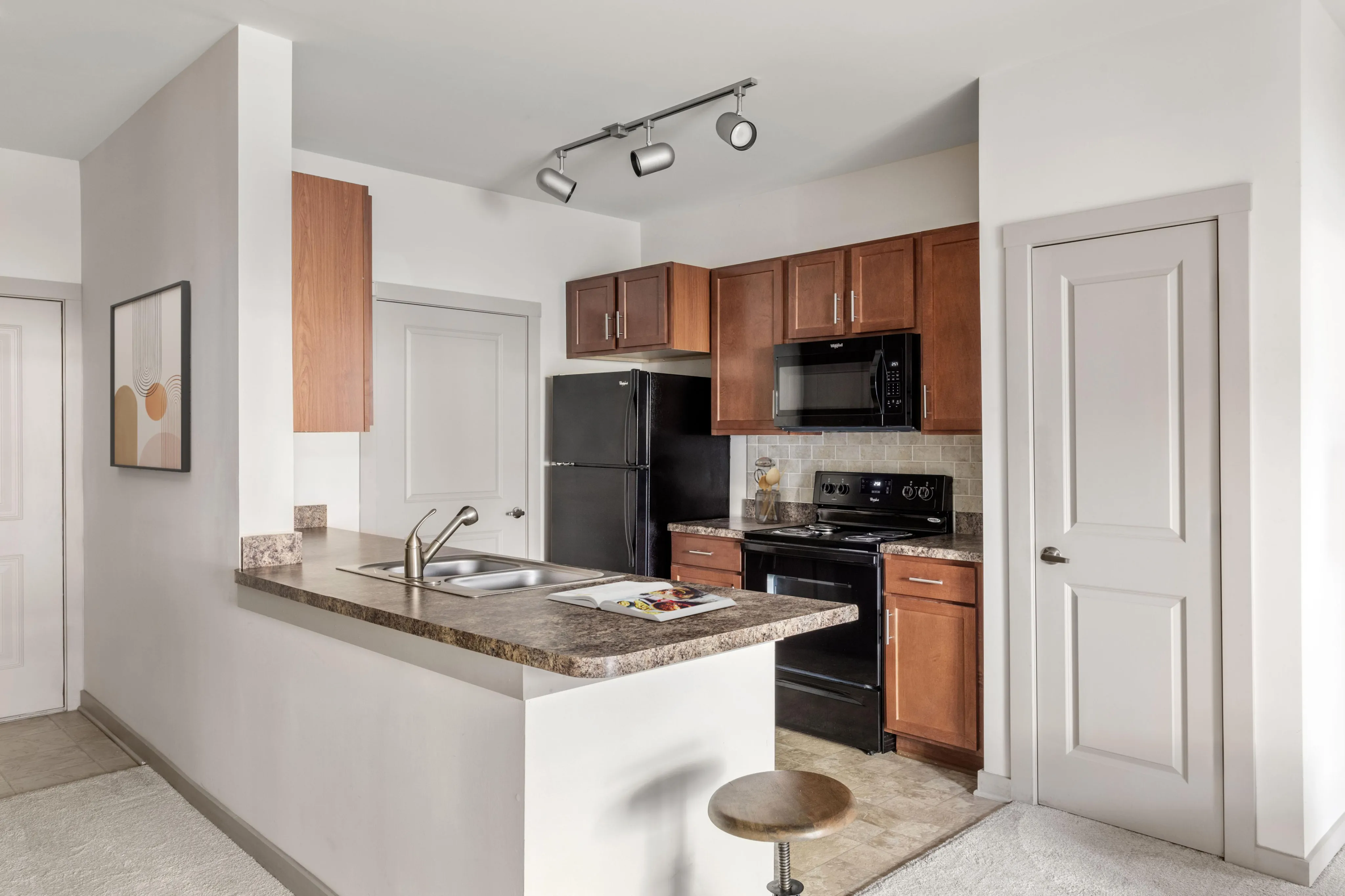 Modern apartment kitchen with sleek countertops, wooden cabinets, and integrated appliances, offering a cozy breakfast bar setting.