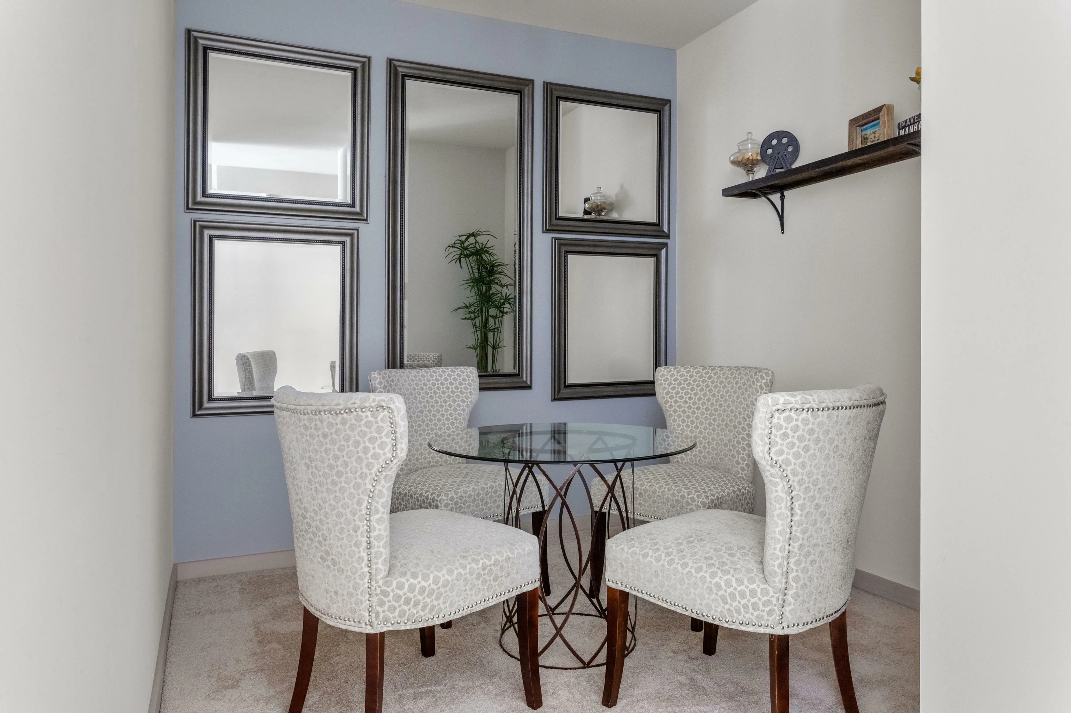 Elegant dining nook featuring a stylish round glass table, four chic patterned chairs, and tasteful wall decor with multiple mirrors.