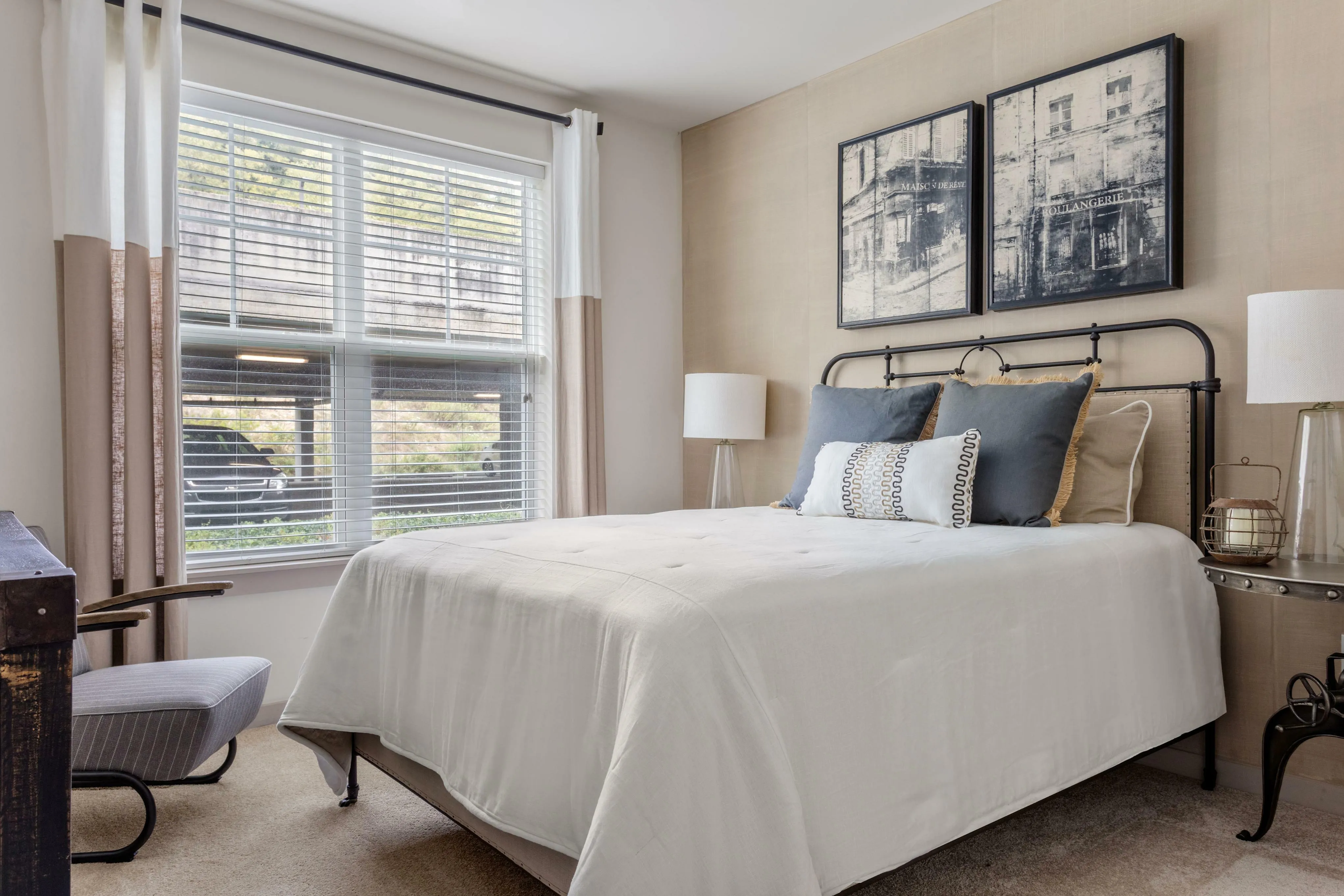 Charming bedroom with elegant decor, showcasing a cozy bed, stylish artwork, and ample natural light from large windows.