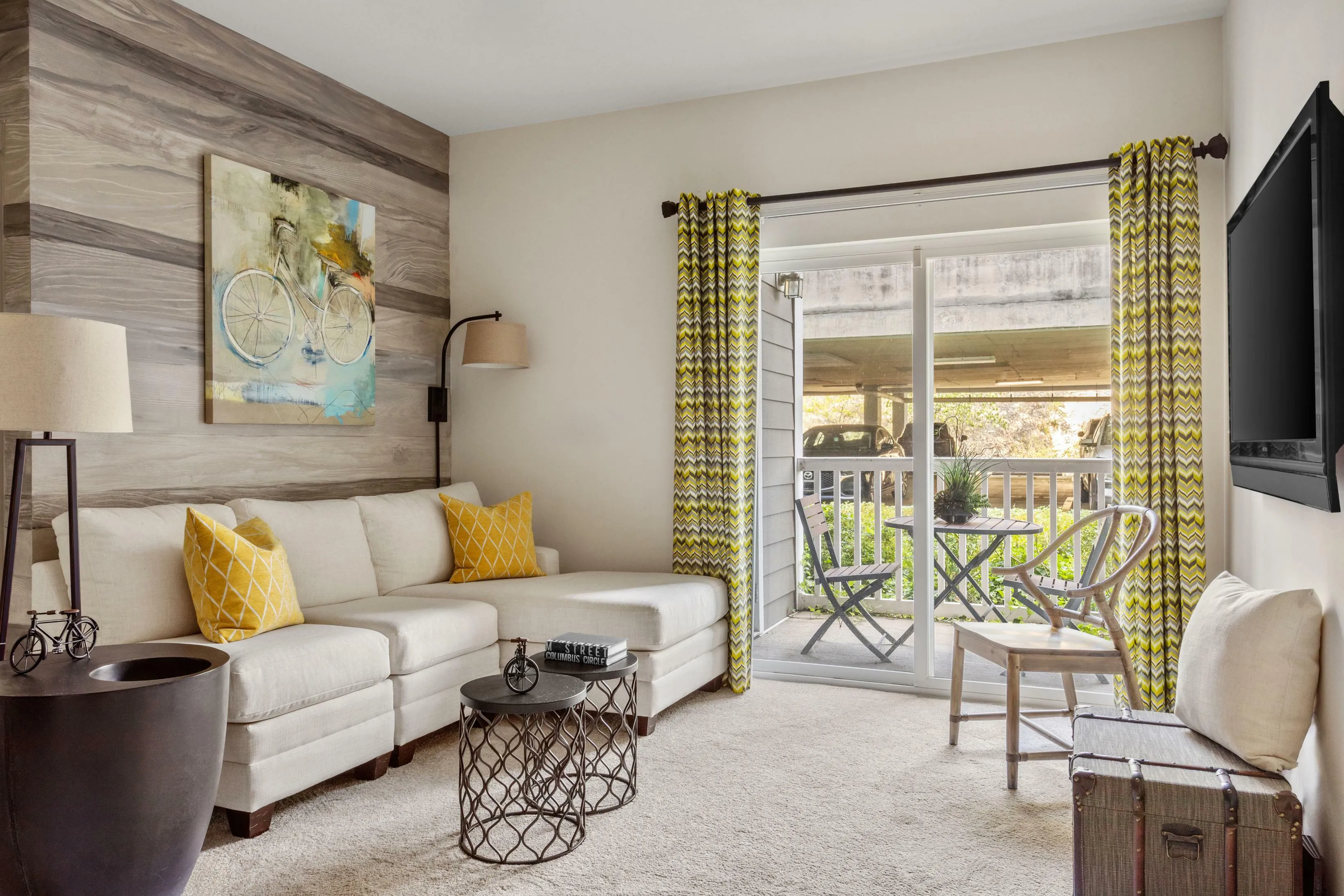 Charming living room with modern decor, vibrant yellow accents, and a cozy couch, opening to a serene patio view.