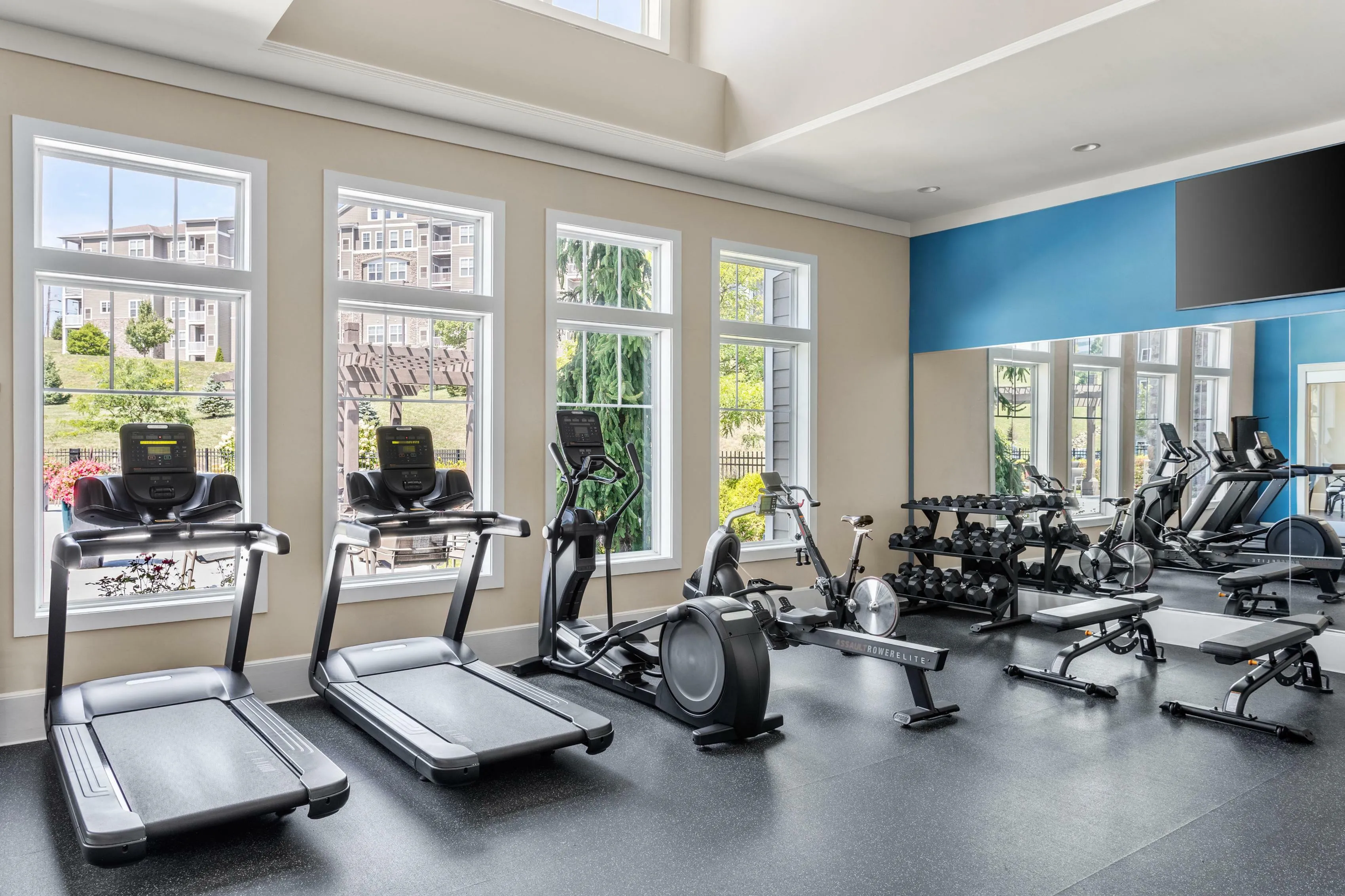 Inviting fitness center with modern equipment, treadmills, elliptical, and weights, enhanced by large windows for natural light.