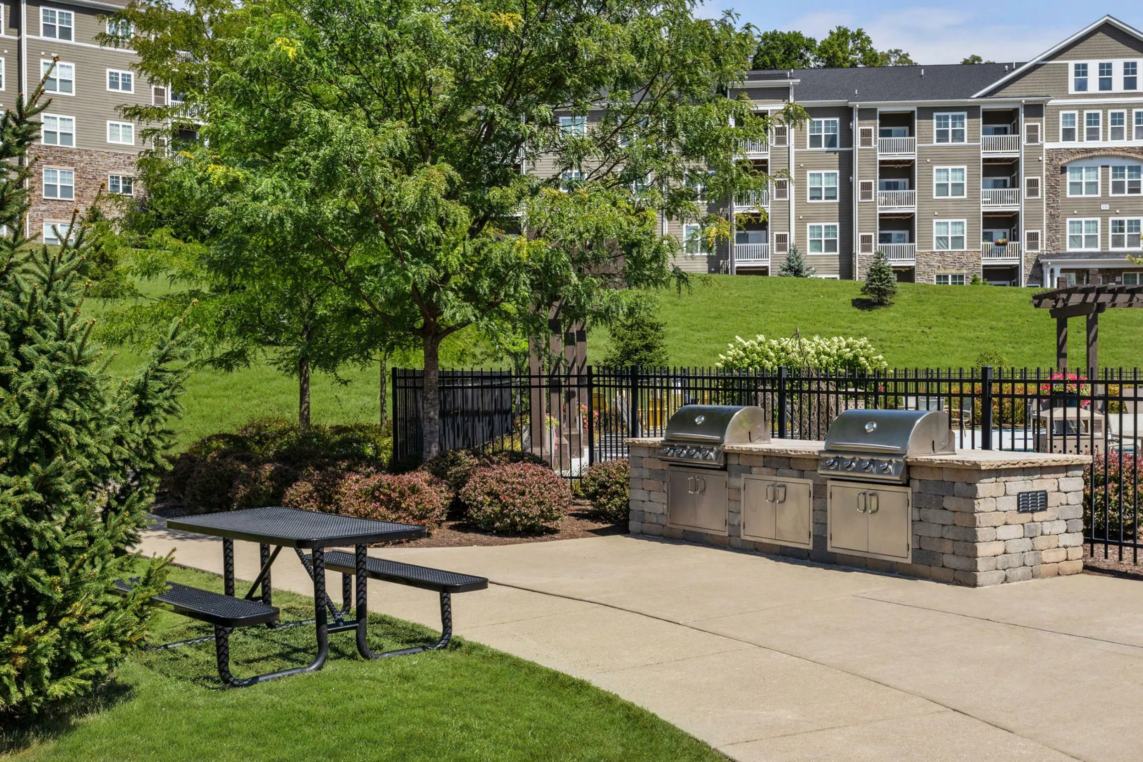 Charming apartment complex featuring outdoor amenities with modern grills, surrounded by lush greenery and scenic views.