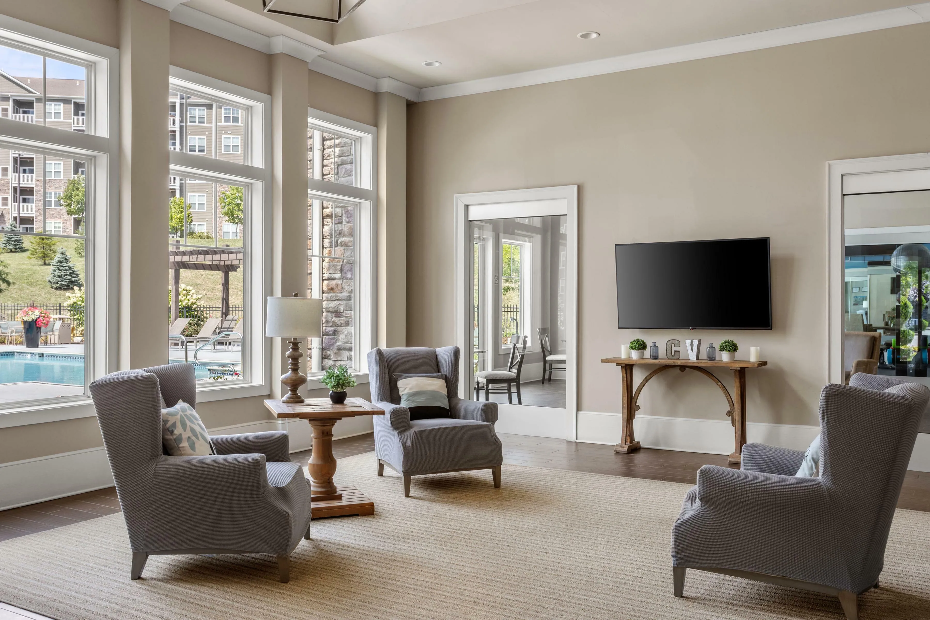 Elegant apartment living room with large windows offering a scenic pool view, stylish armchairs, and a modern wall-mounted TV.