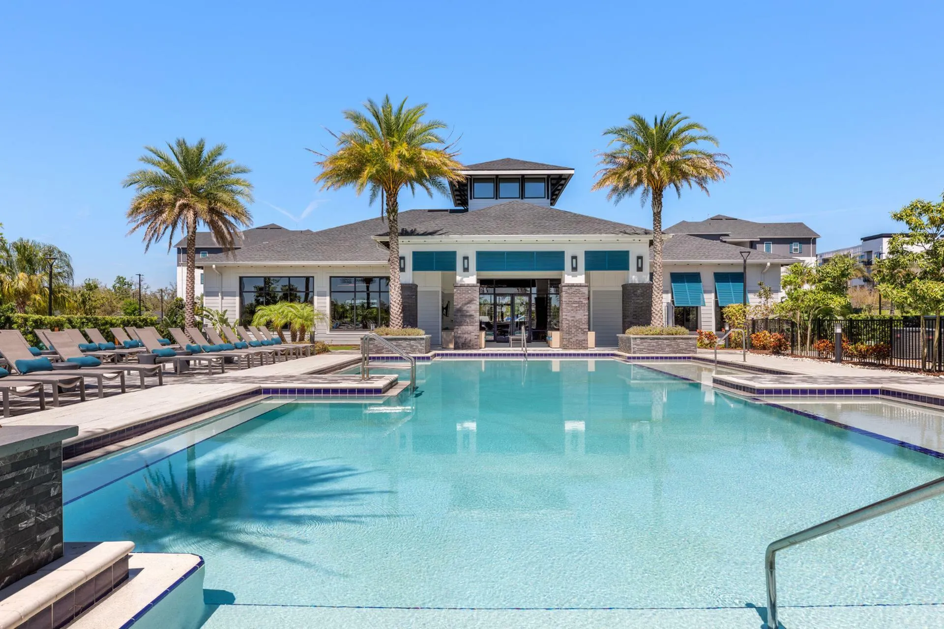 Luxurious resort-style swimming pool with sun loungers and palm trees in a vibrant apartment community setting.