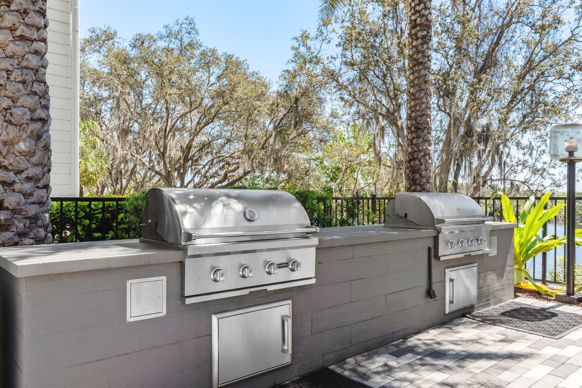 Luxurious outdoor grilling area with twin stainless steel BBQs surrounded by lush greenery and scenic views.