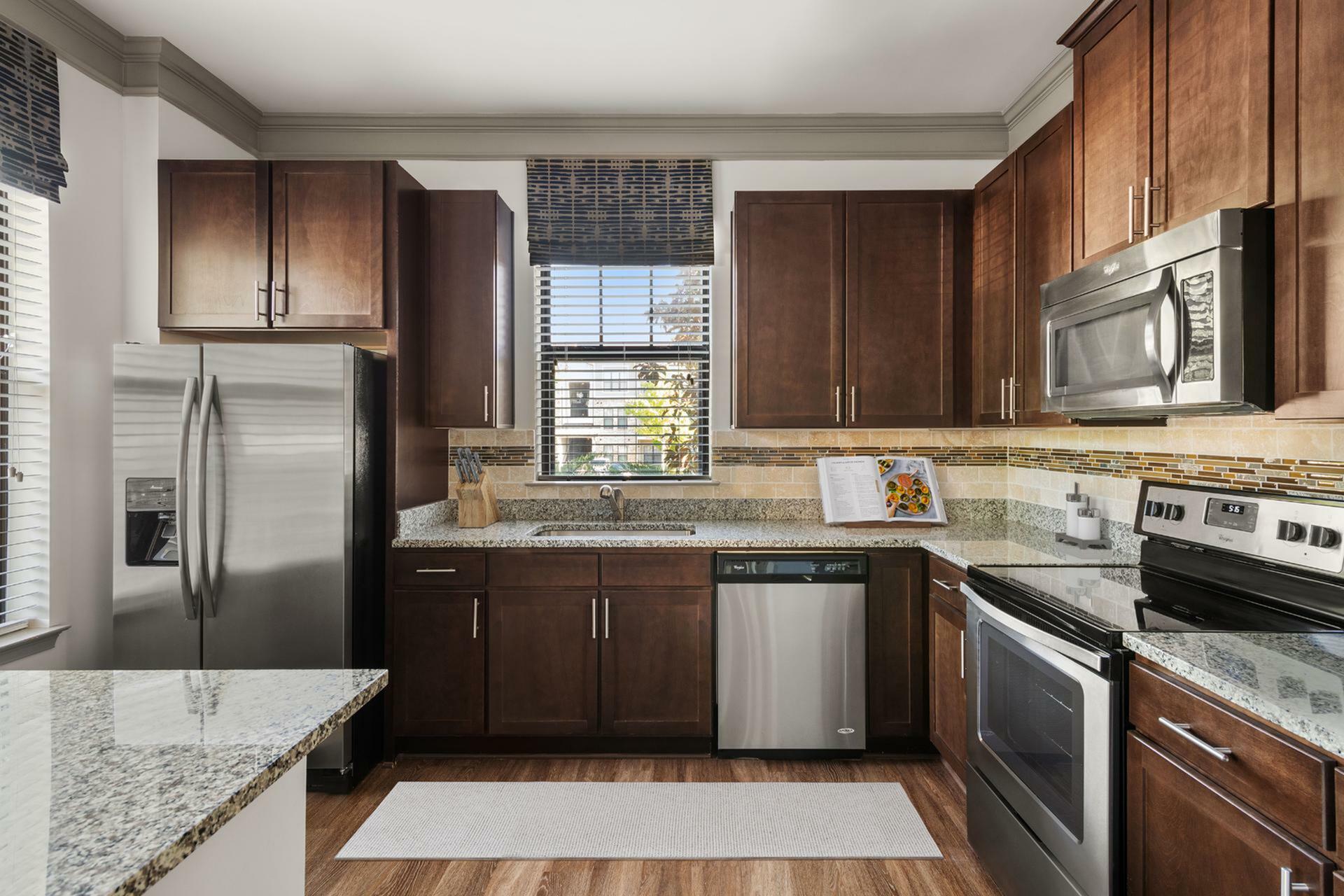 Modern kitchen with sleek stainless steel appliances, granite countertops, and rich wooden cabinetry, offering a stylish and functional space.