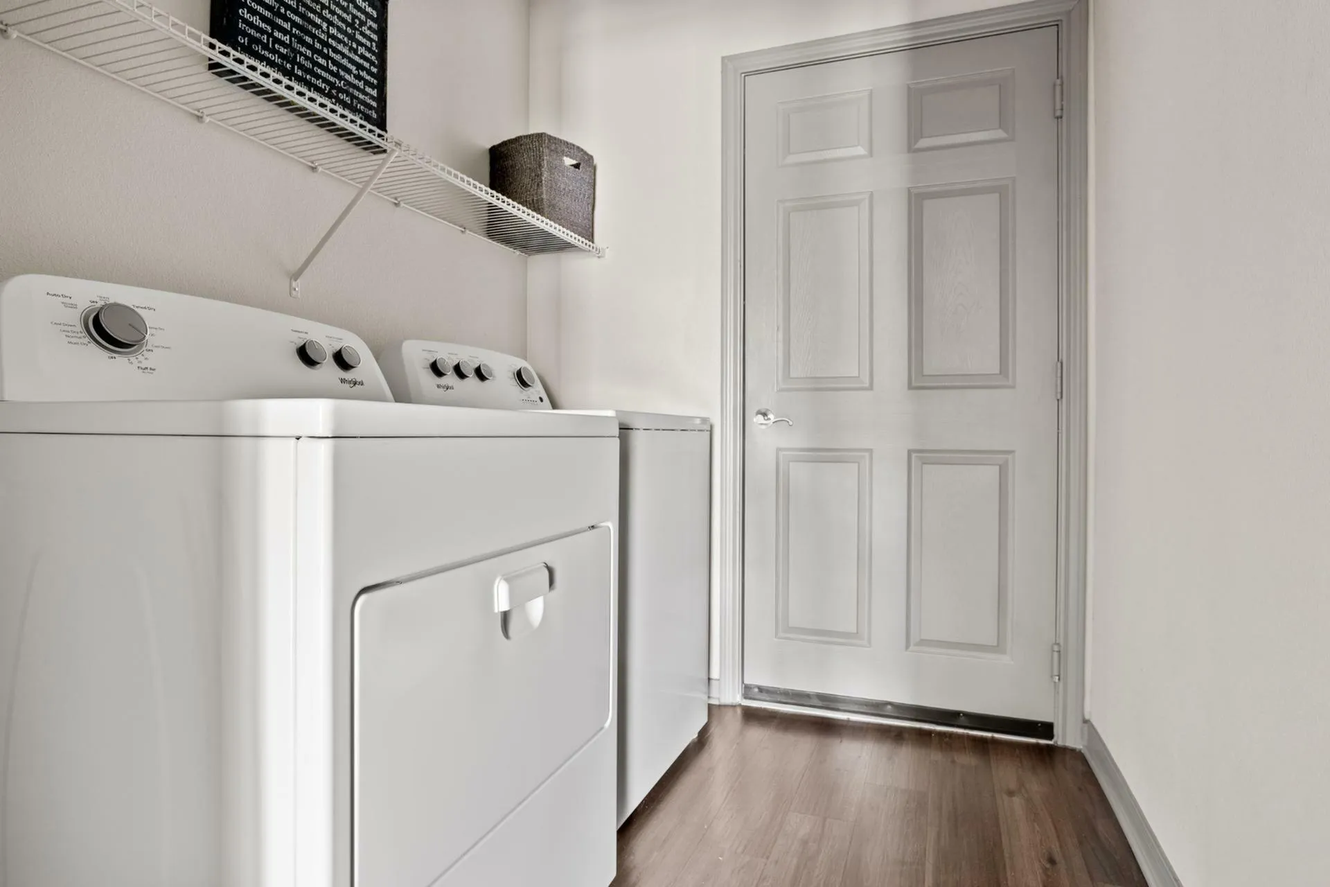 Modern laundry room with sleek washer and dryer, elegant shelving, and hardwood flooring.