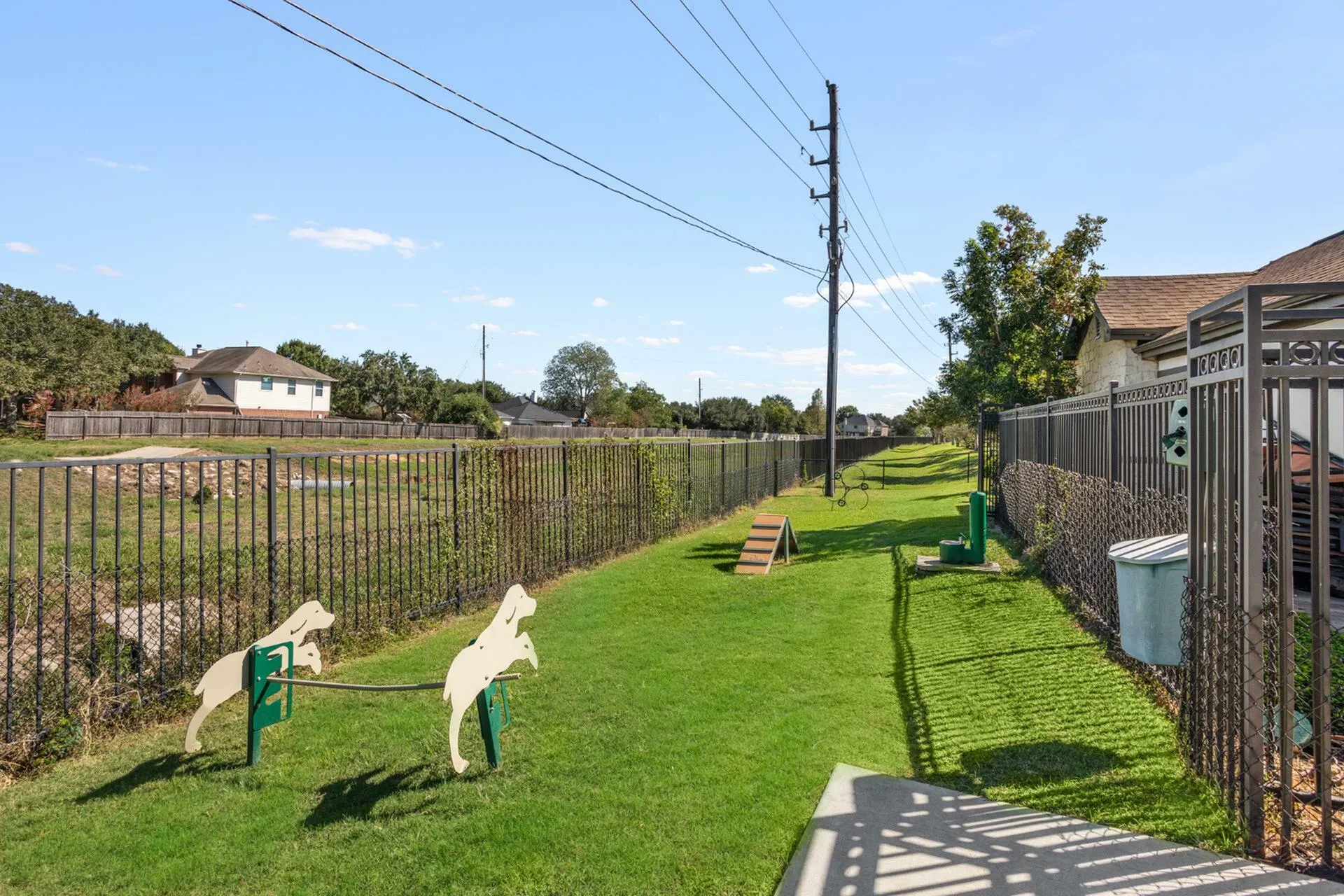 Inviting green outdoor space with exercise equipment for dogs, surrounded by charming wooden houses and clear blue skies.