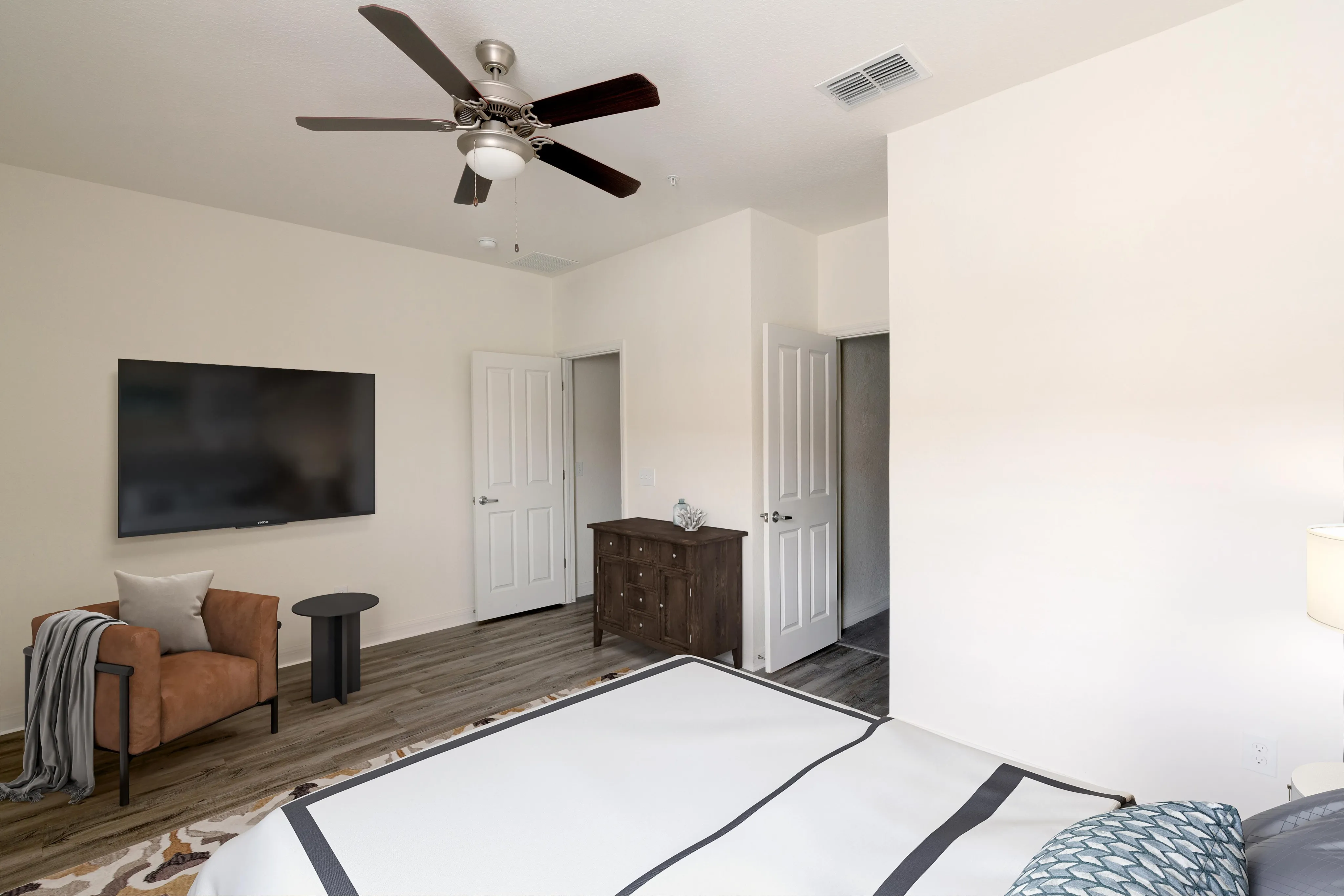 Elegant bedroom featuring a mounted flat-screen TV, plush armchair, and modern ceiling fan with sleek wood flooring.