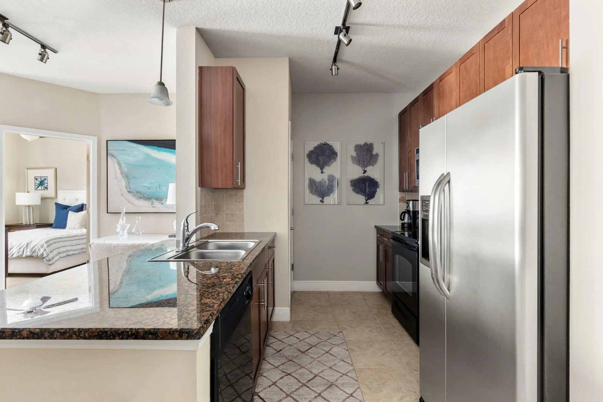 Modern kitchen with sleek stainless steel appliances, granite countertops, and stylish wooden cabinets, opening to a cozy bedroom with elegant decor.