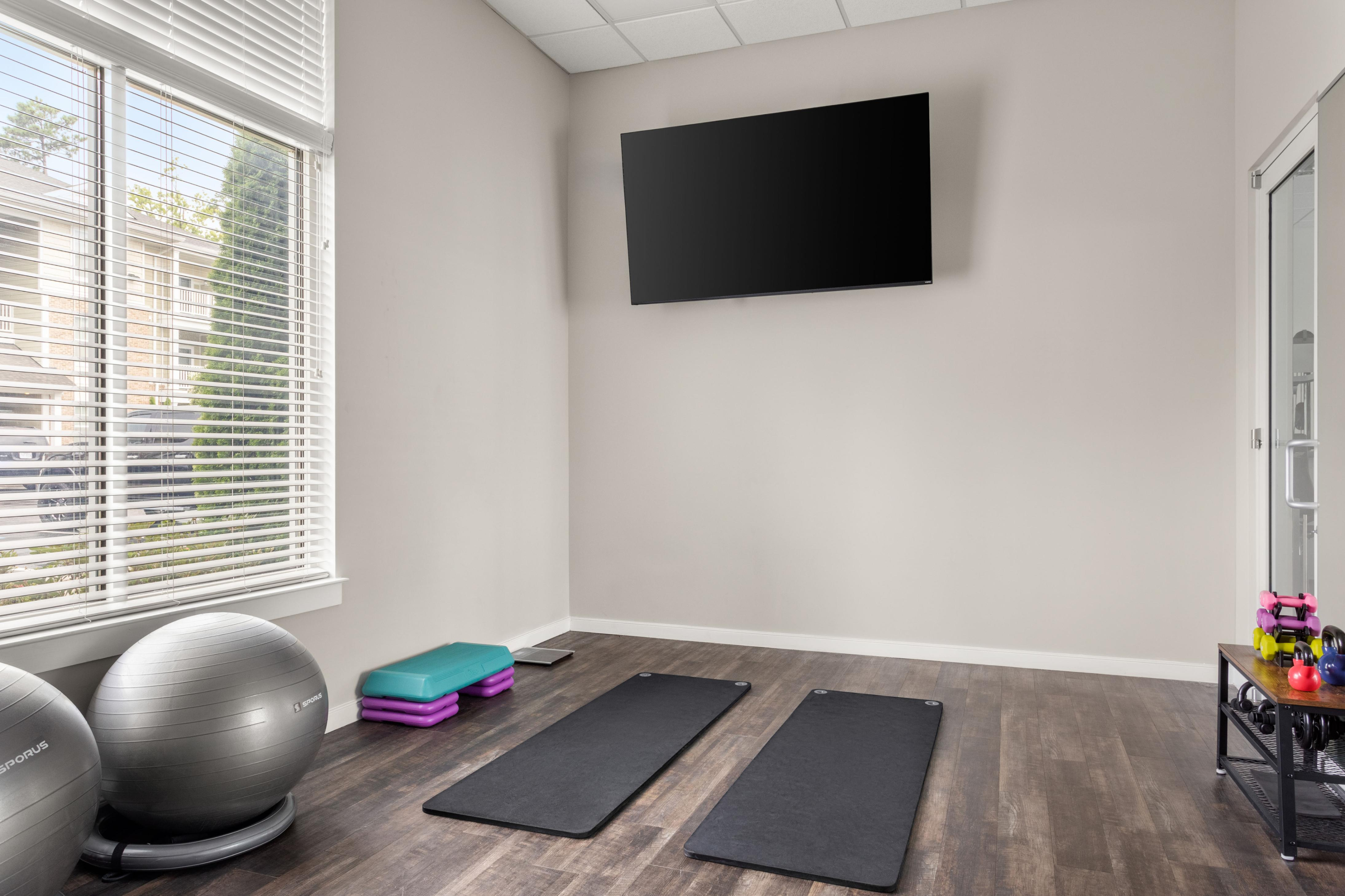 Inviting home gym space with modern exercise equipment, large windows for natural light, and a sleek wall-mounted TV.