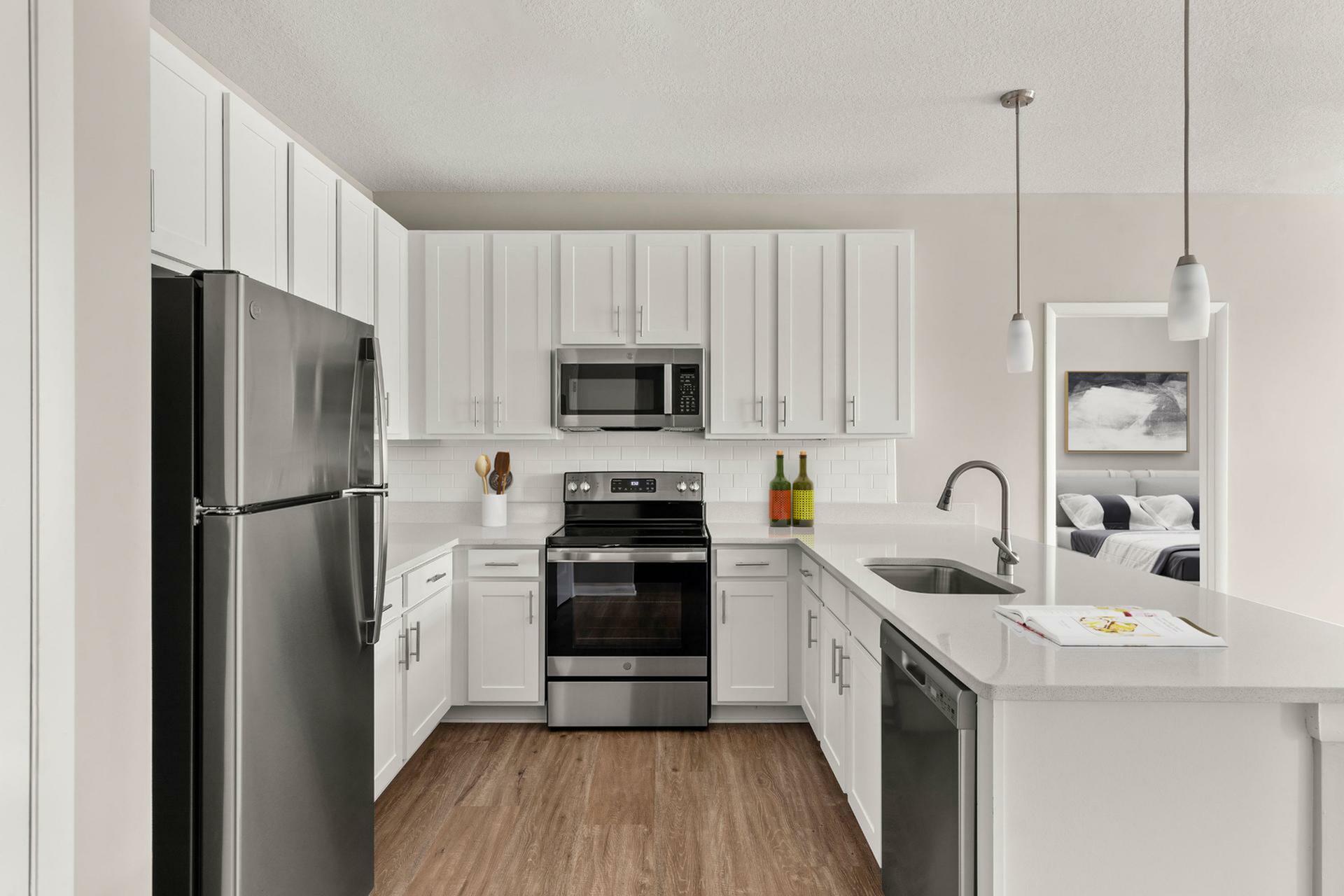 Modern kitchen with sleek stainless steel appliances, elegant white cabinetry, and hardwood floors, leading into a cozy bedroom.