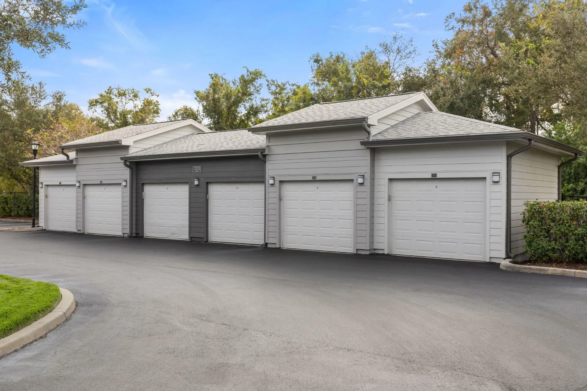 Modern garage units with sleek white doors set in a serene, tree-lined community.