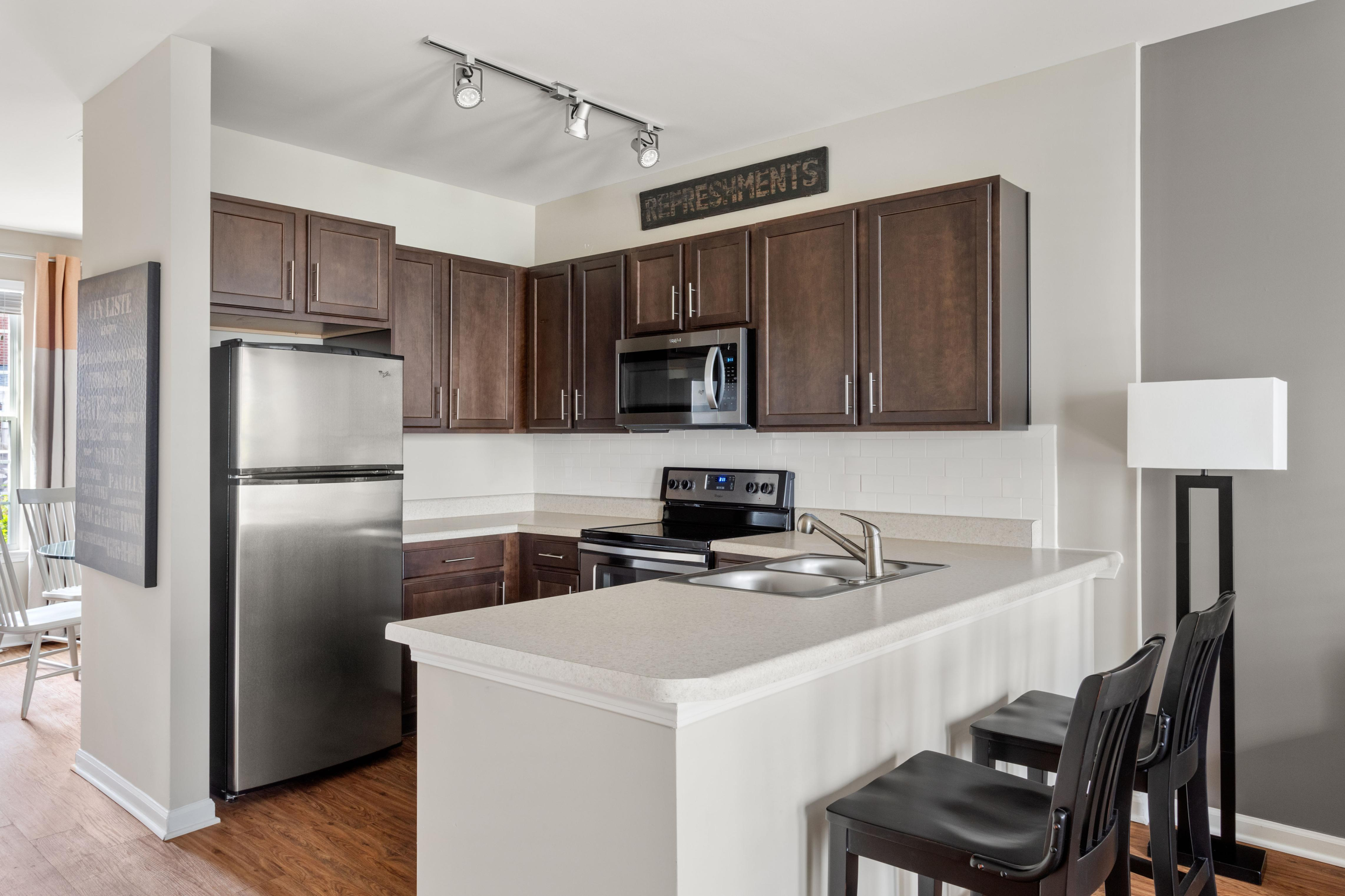 Elegant kitchen with rich wood cabinetry, stainless steel appliances, and a cozy breakfast bar with seating, perfect for modern living.