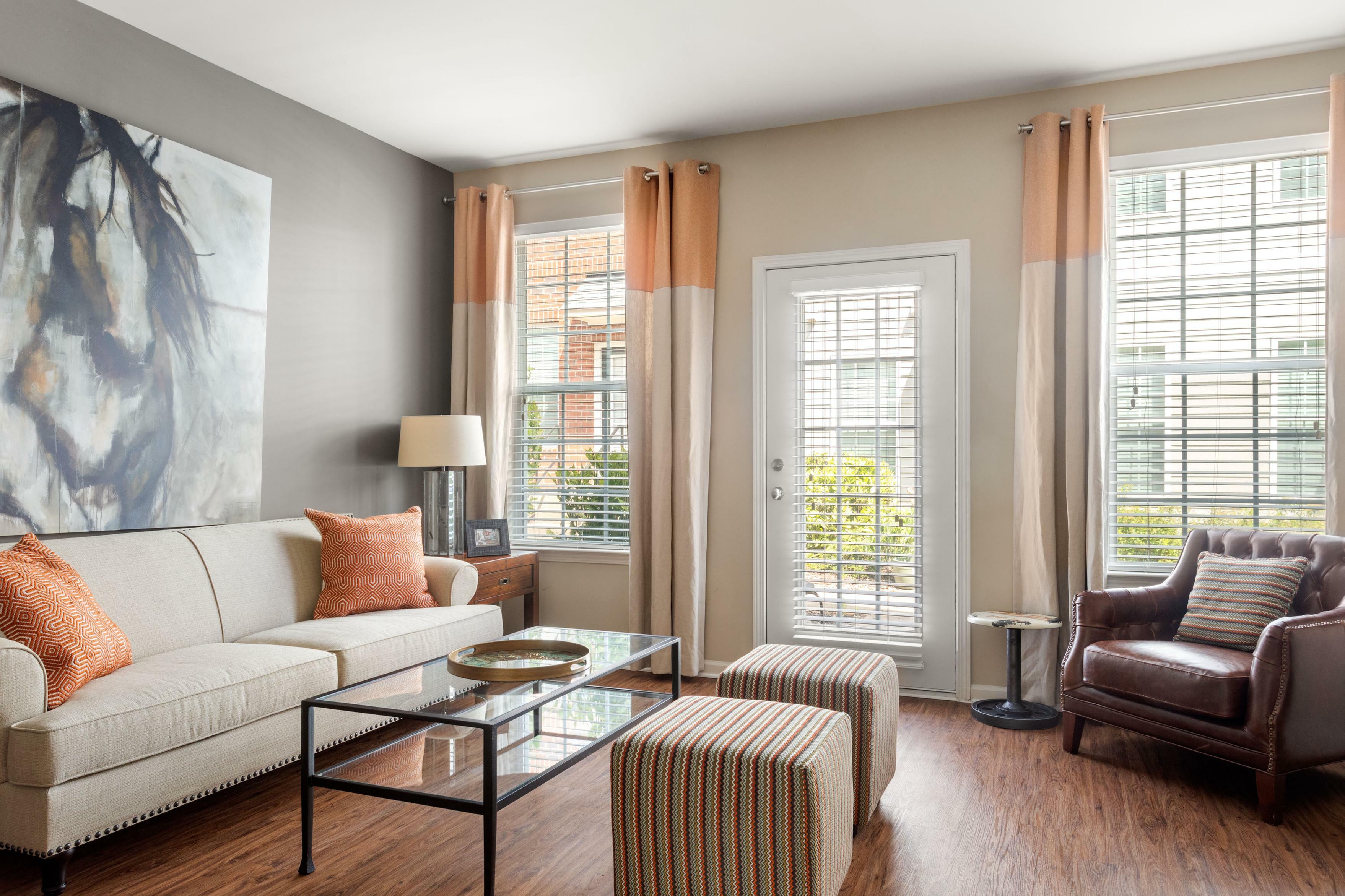 Inviting living room with elegant beige sofa, vibrant orange cushions, stylish glass coffee table, and rich wooden flooring, perfect for cozy relaxation.