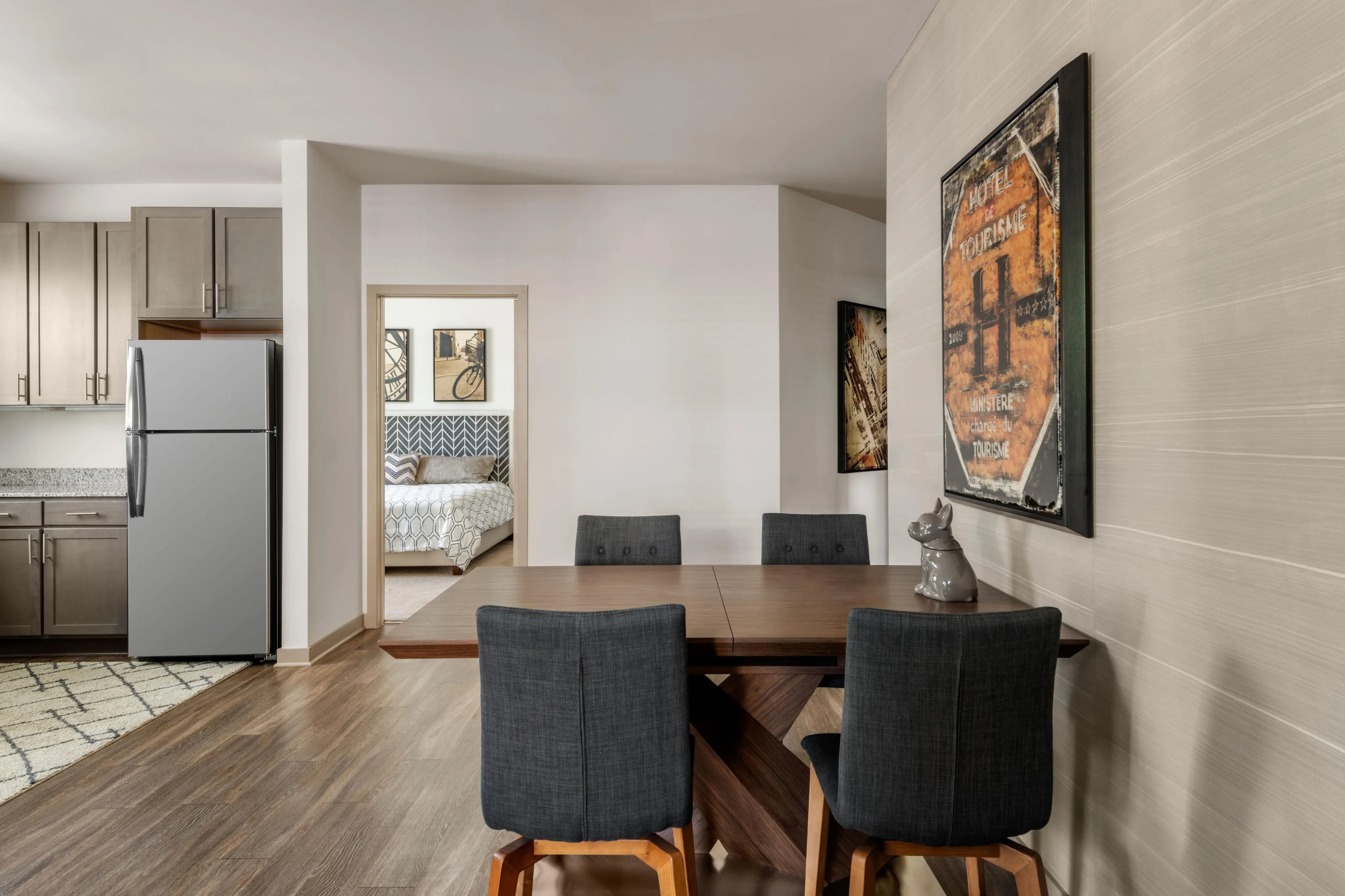 Modern apartment interior featuring a cozy dining area with stylish chairs, a sleek kitchen with stainless steel appliances, and a glimpse of a comfortable bedroom with chic decor.
