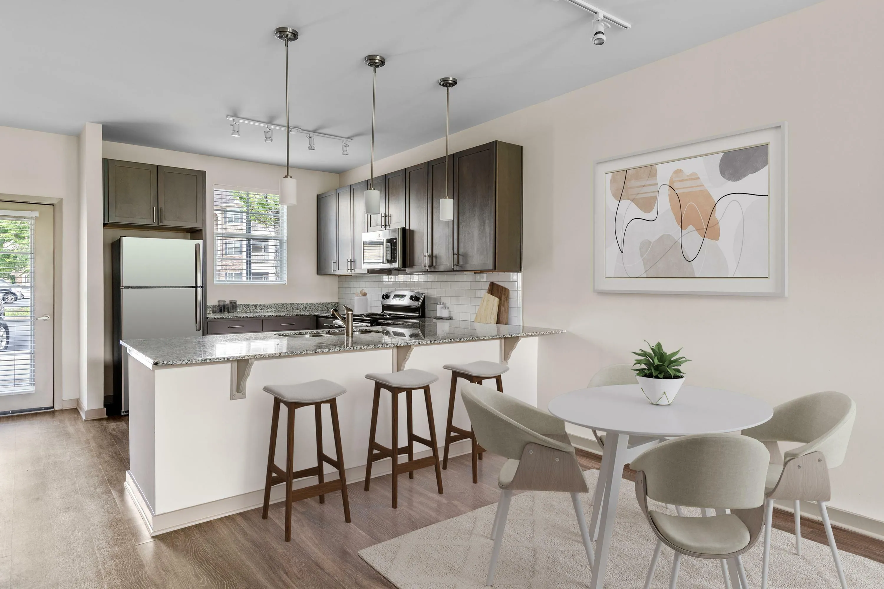 Modern kitchen with sleek granite countertops, stylish bar stools, and contemporary art enhancing a bright dining area.