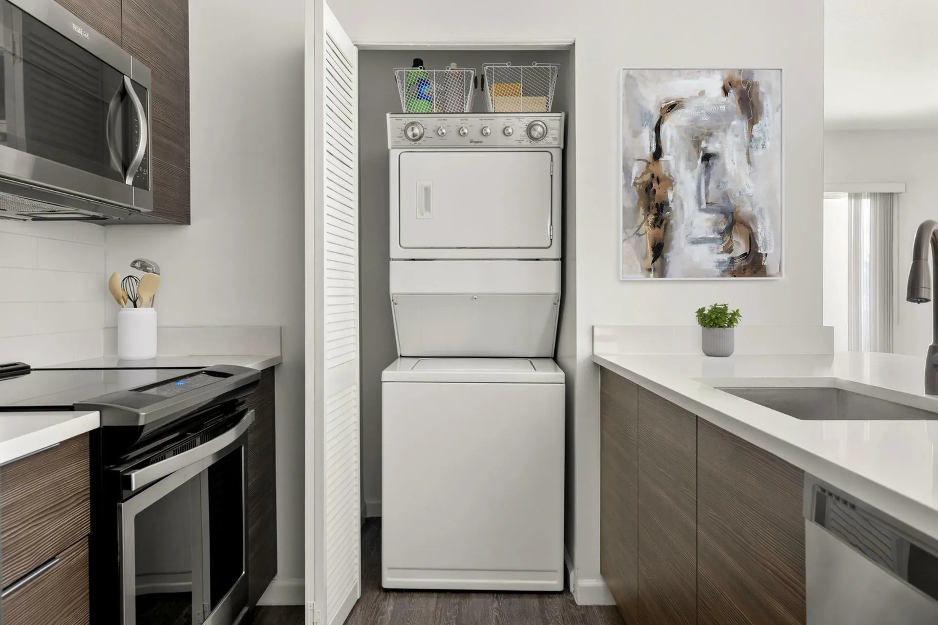 Modern kitchen with sleek cabinetry, integrated washer-dryer, and stylish countertop, featuring contemporary artwork and a touch of greenery.
