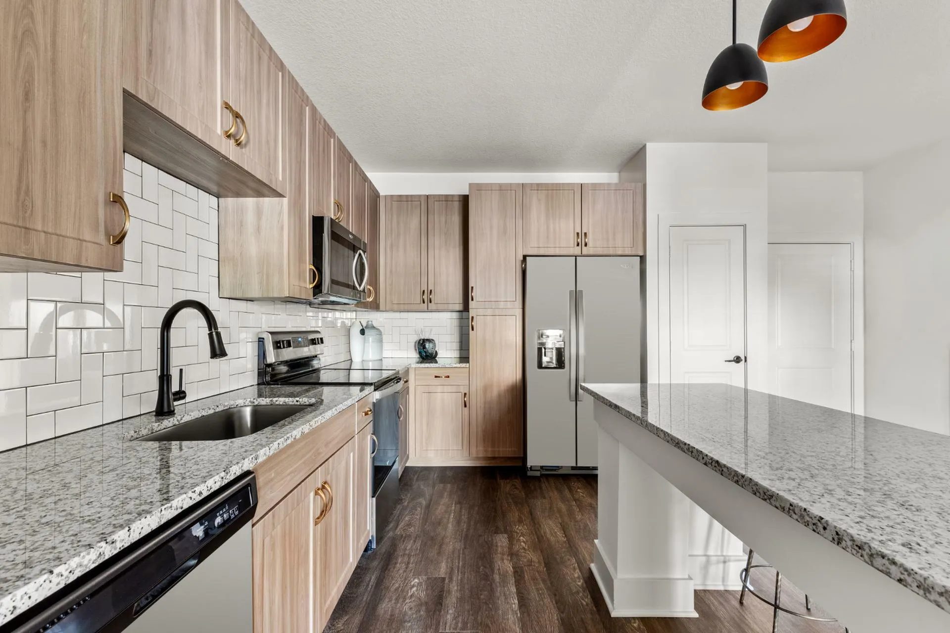 Modern kitchen design with elegant wood cabinetry, sleek granite countertops, and stainless steel appliances, complemented by stylish pendant lighting.
