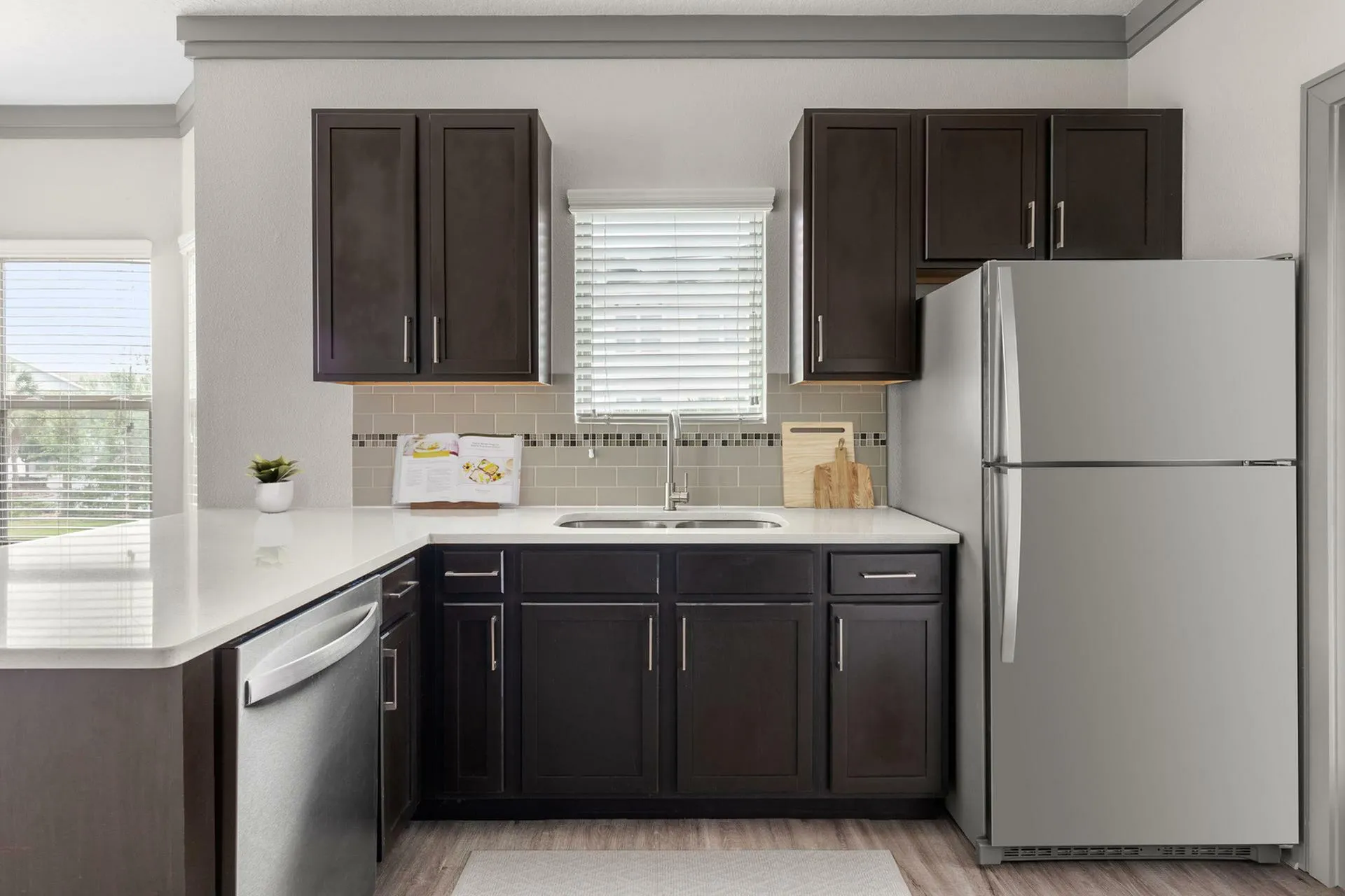Modern kitchen with dark wood cabinets, sleek countertops, and stainless steel appliances, bathed in natural light.