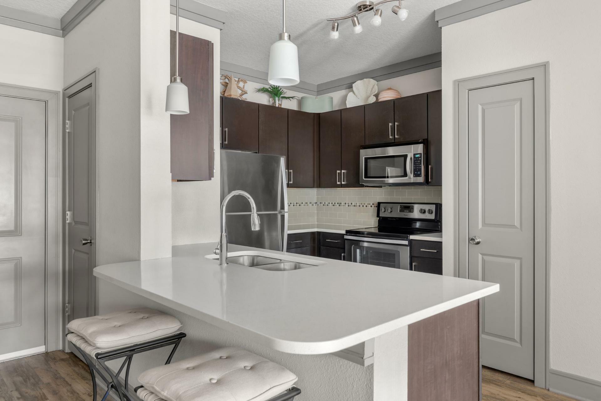 Contemporary kitchen with sleek dark cabinets, modern stainless steel appliances, and an elegant breakfast bar with cushioned seating.