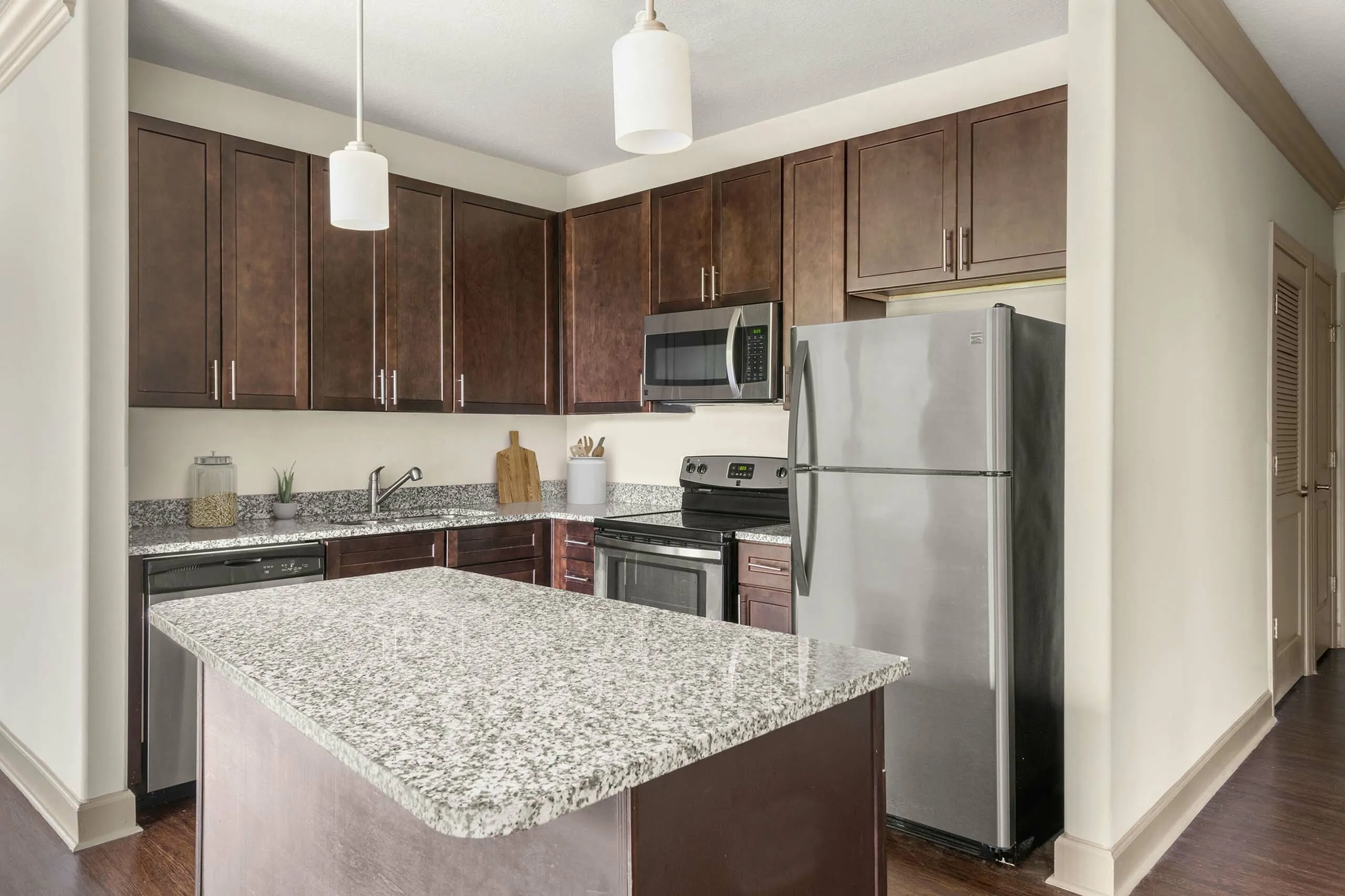 Elegant kitchen with dark wood cabinets, granite countertops, and stainless steel appliances, featuring a central island under modern pendant lighting.