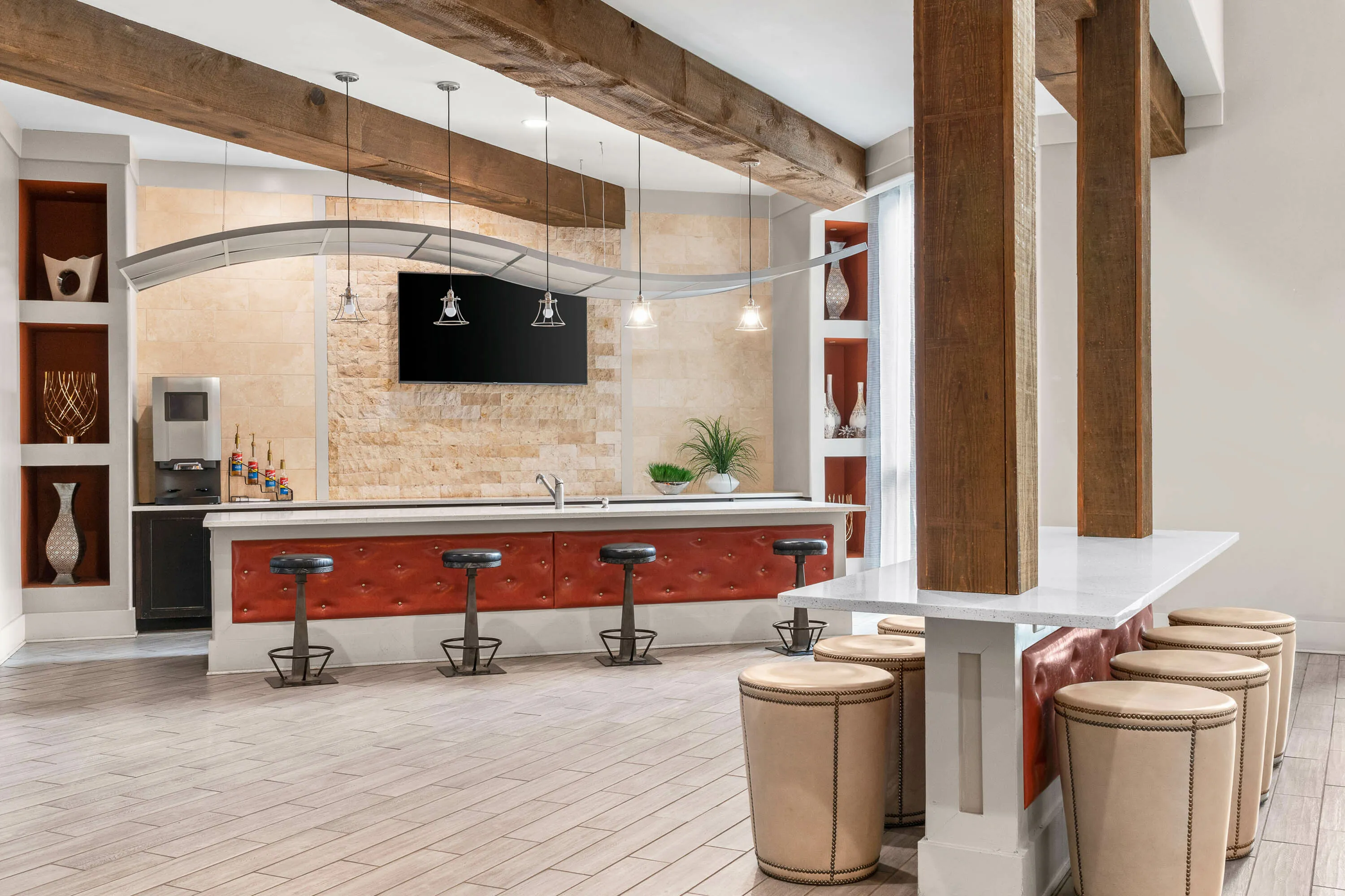 Chic modern kitchen area with plush red seating, industrial bar stools, and sleek decor under rustic wooden beams.