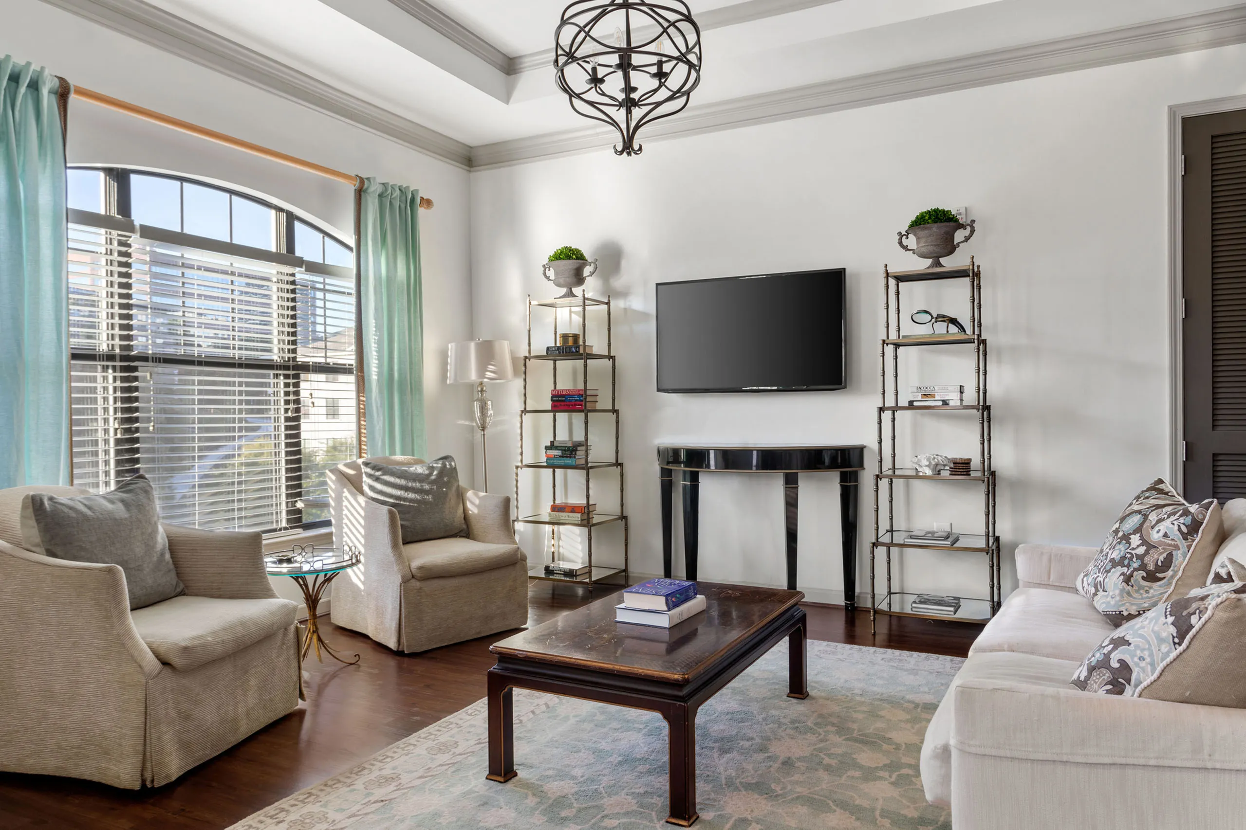 Elegant living room with plush seating, natural light, and modern decor, featuring a flat-screen TV and chic shelving.