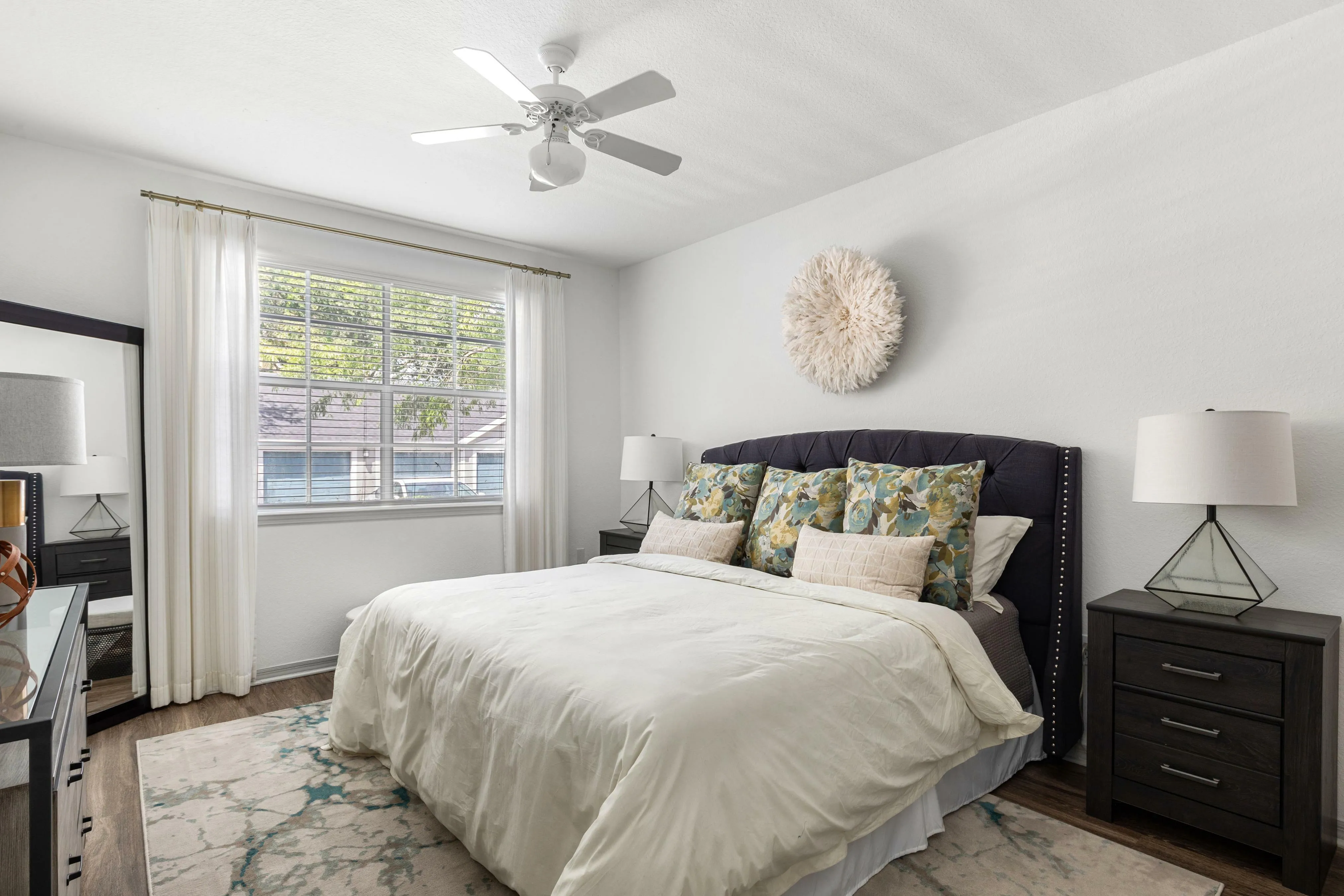 Bright and airy bedroom featuring a plush bed with decorative pillows, elegant nightstands, and large window draped with sheer curtains, offering a tranquil retreat.