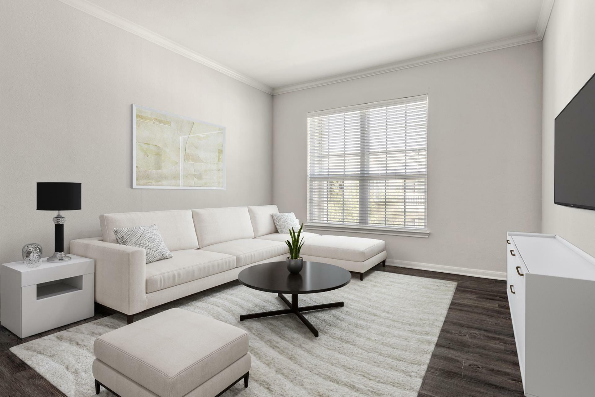 Modern and inviting living room with elegant white sectional sofa, sleek floor lamp, and stylish round coffee table on a plush carpet, featuring large window with blinds for natural light.